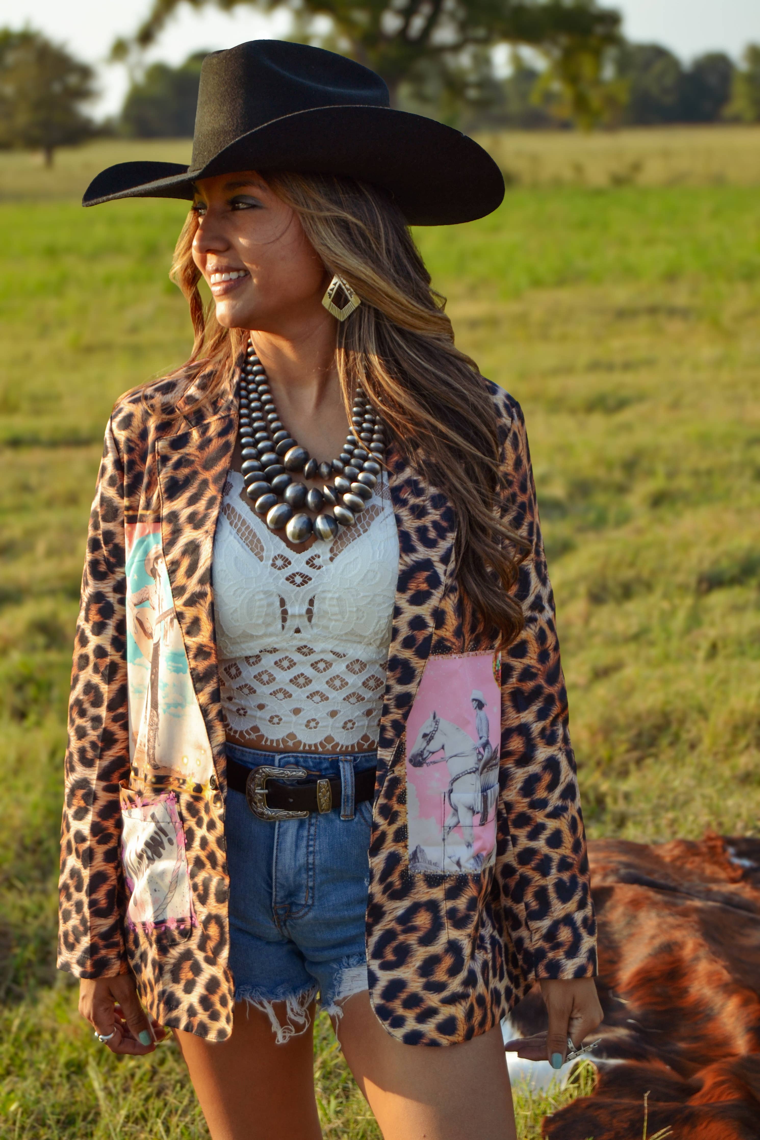 Woman in a leopard print jacket standing in a field with a cow.
