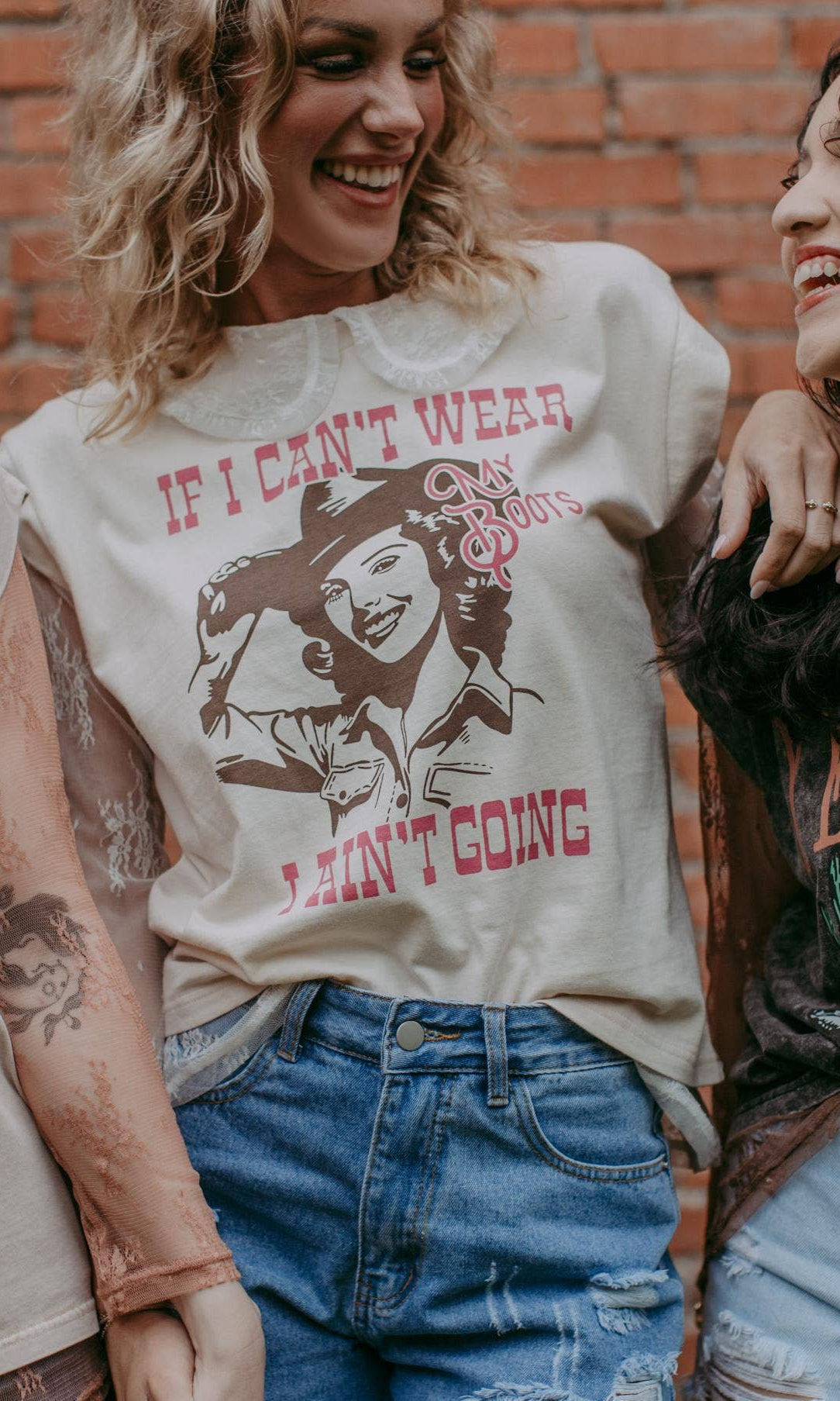 Three women wearing vintage-style t-shirts with cowboy graphics against a brick wall.