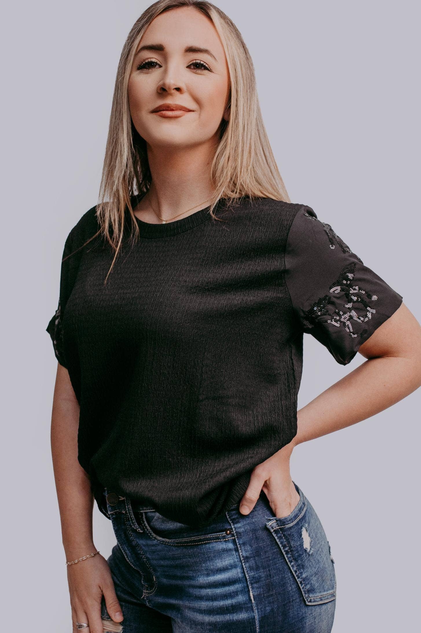 Woman wearing a black t-shirt with horse sequin details against a plain background