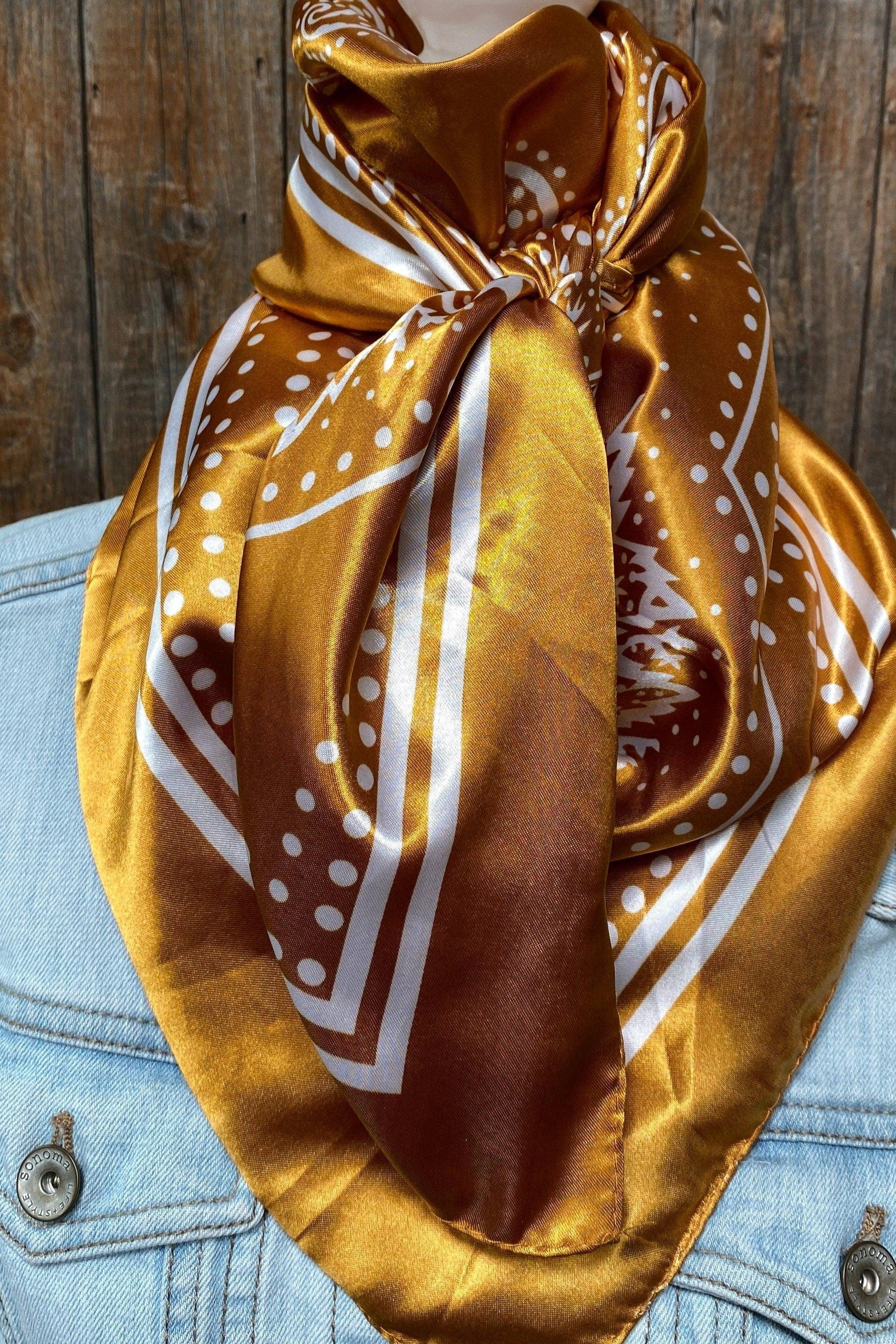 Mustard yellow patterned scarf draped over a denim jacket against a wooden background