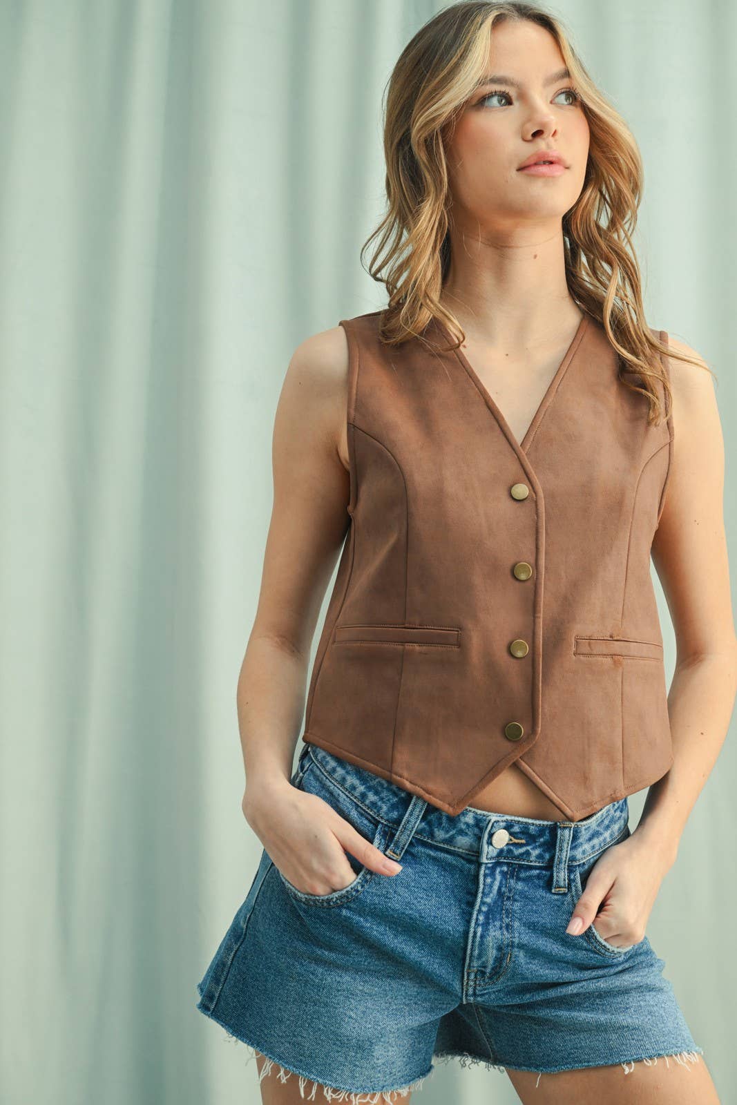 A woman wearing a camel suede button-up vest over a white shirt, paired with a leopard print mini skirt.