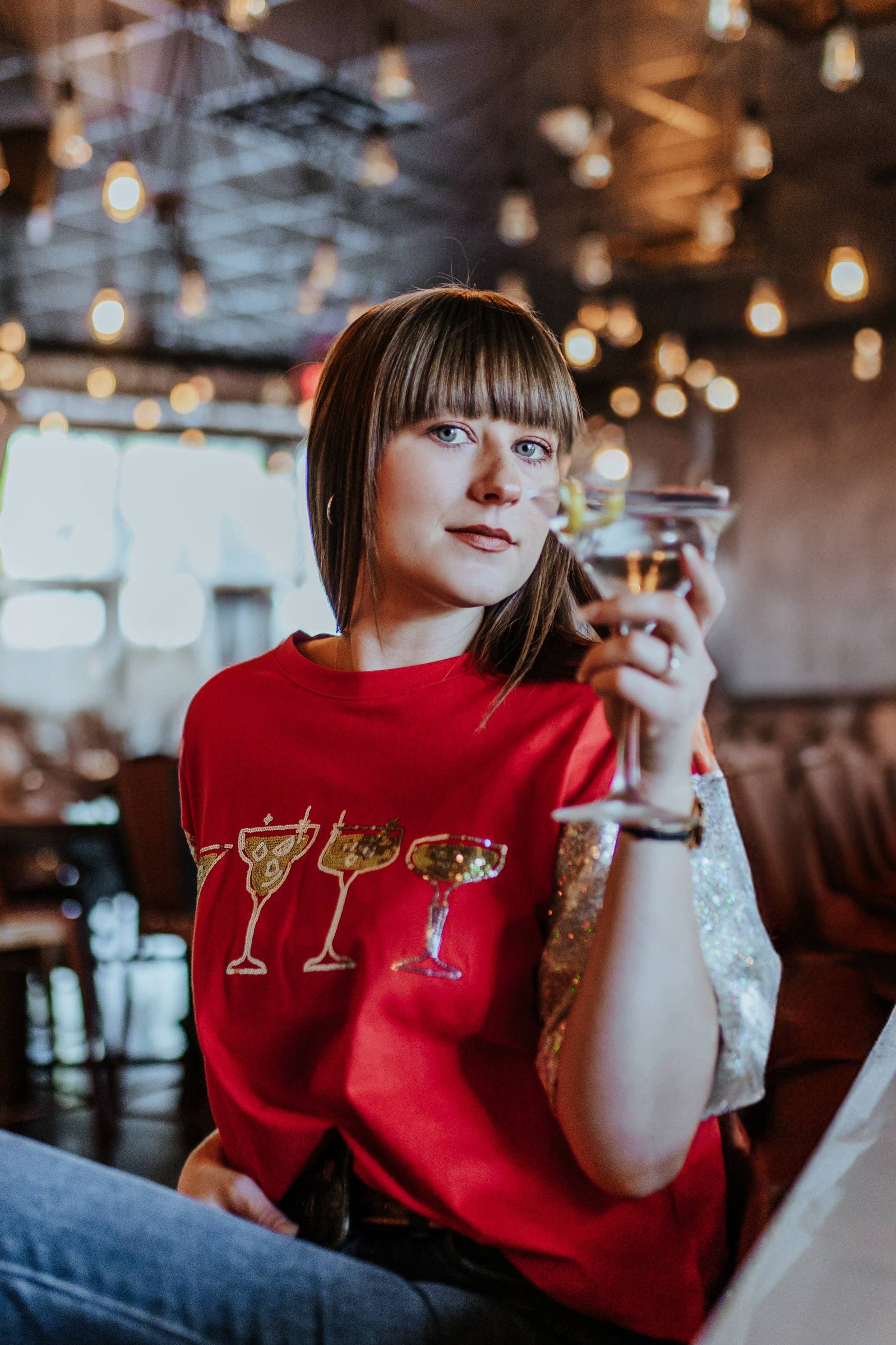 Person in a red shirt with drink designs sitting at a bar counter.