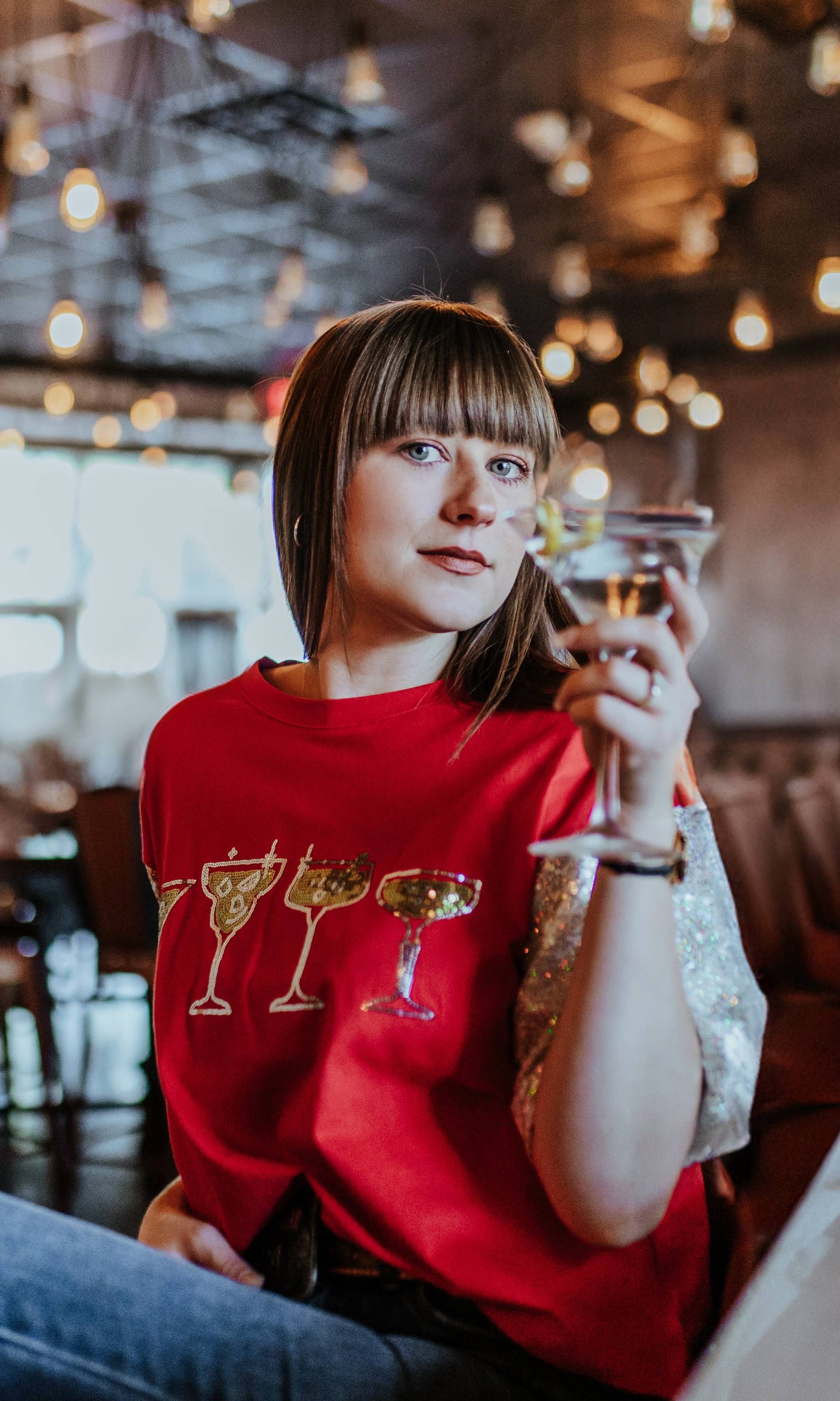 Person in a red shirt with drink designs sitting at a bar counter.