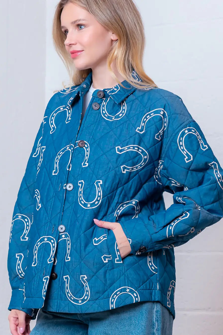Front view of denim-blue quilted jacket with white horseshoe print and button front on model.