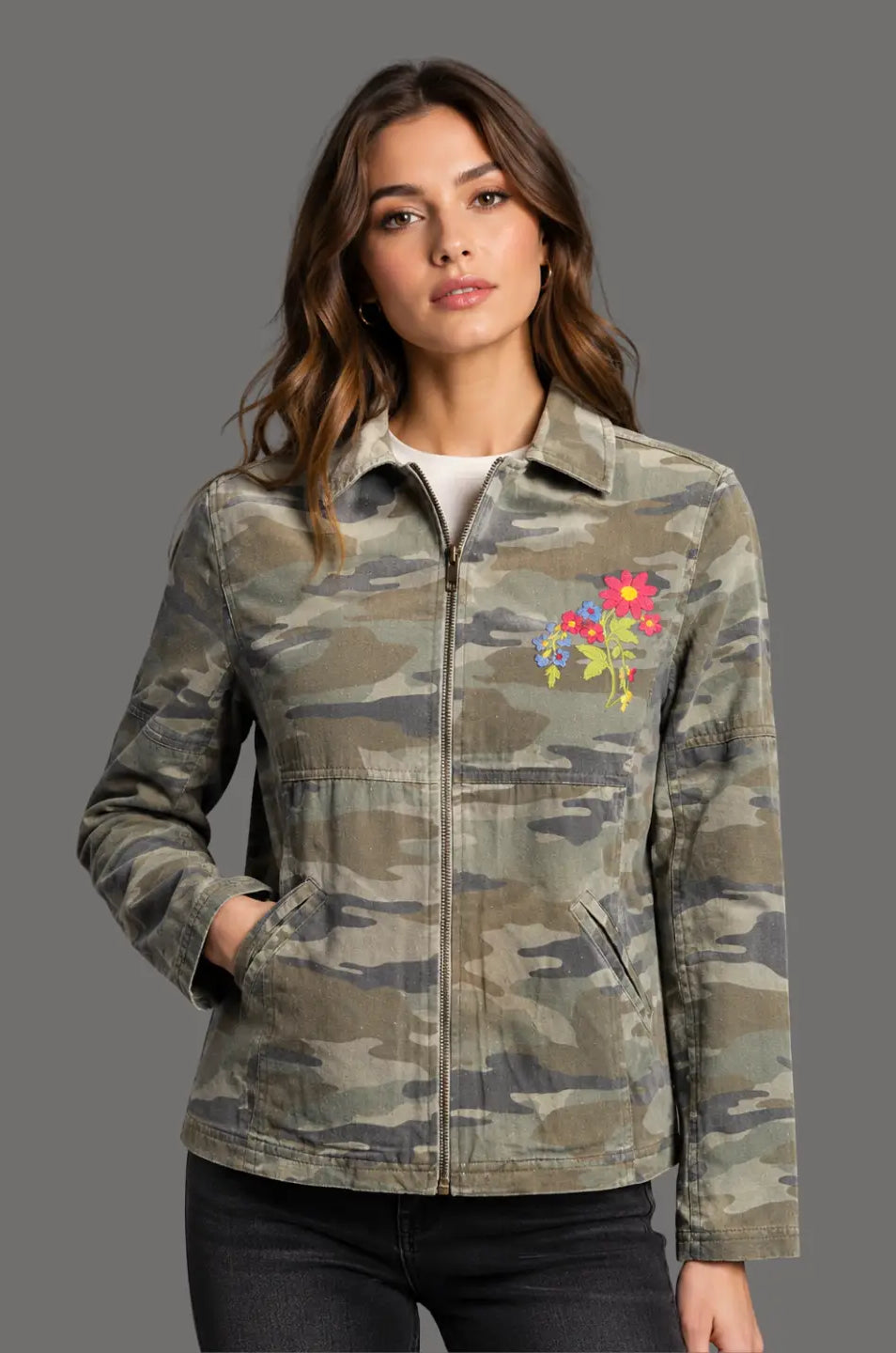 Woman wearing a camouflage jacket with a colorful floral patch on a gray background
