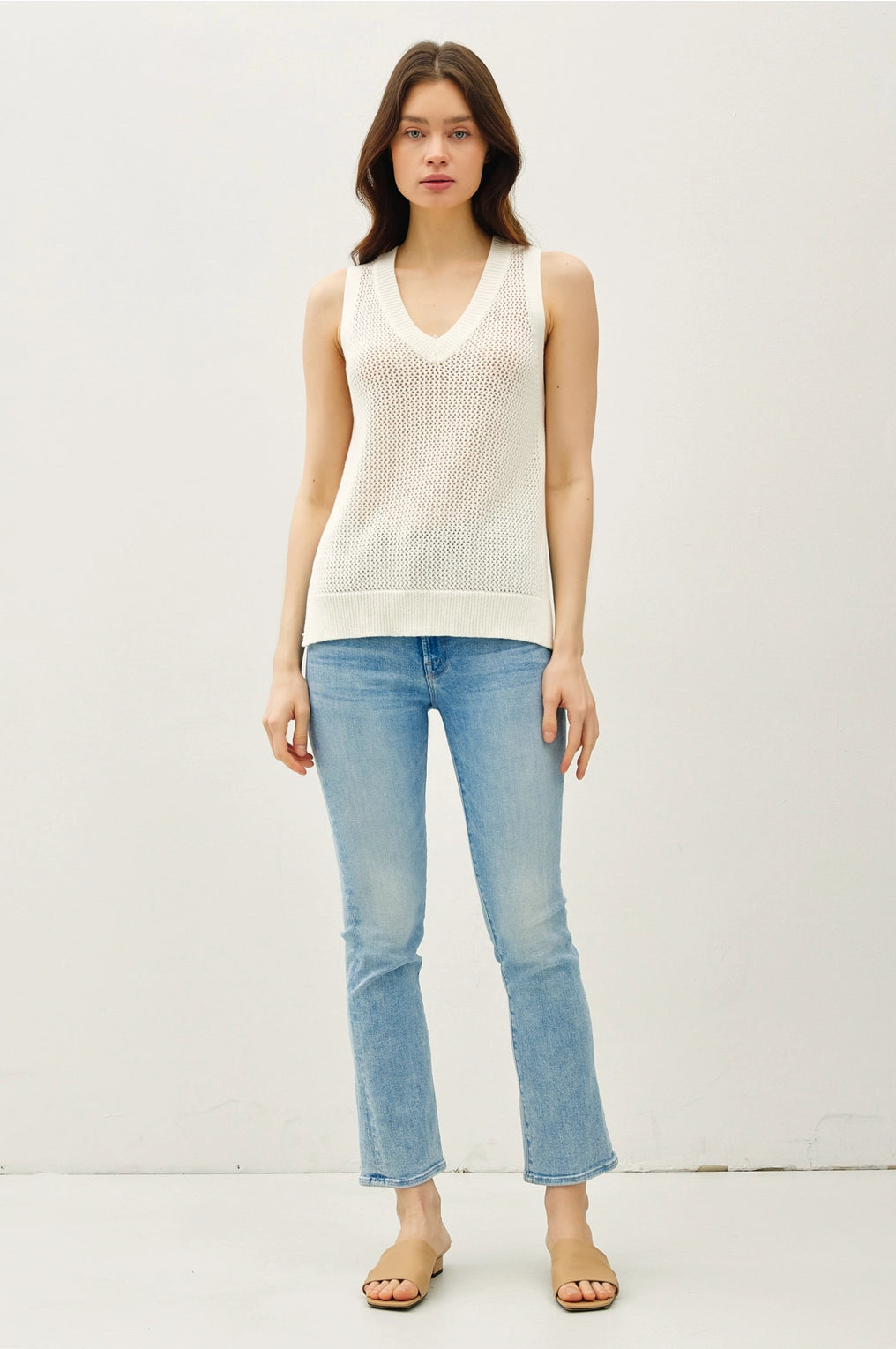 Woman wearing a white sleeveless top and light blue jeans on a white background