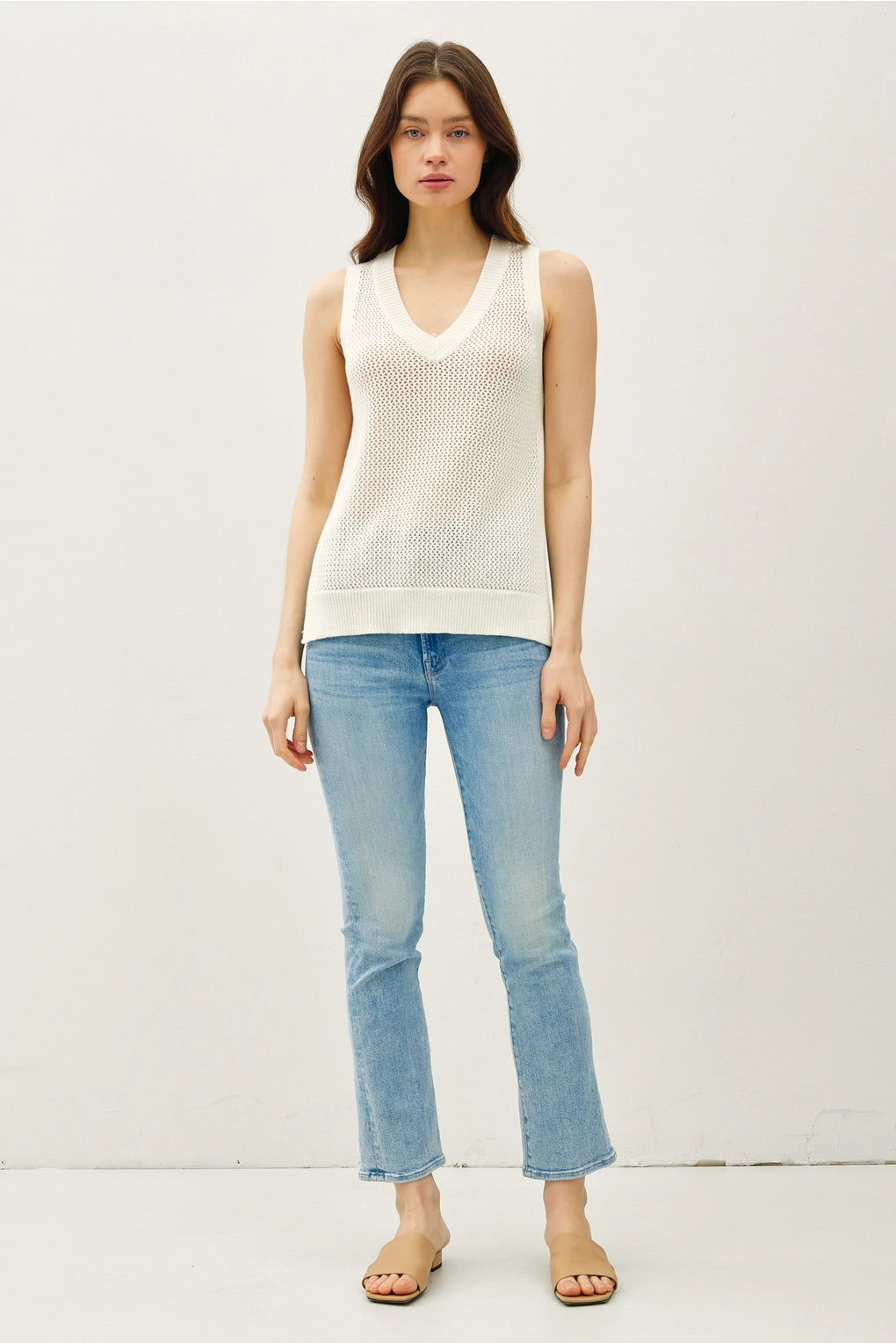 Woman wearing a white sleeveless top and light blue jeans on a white background