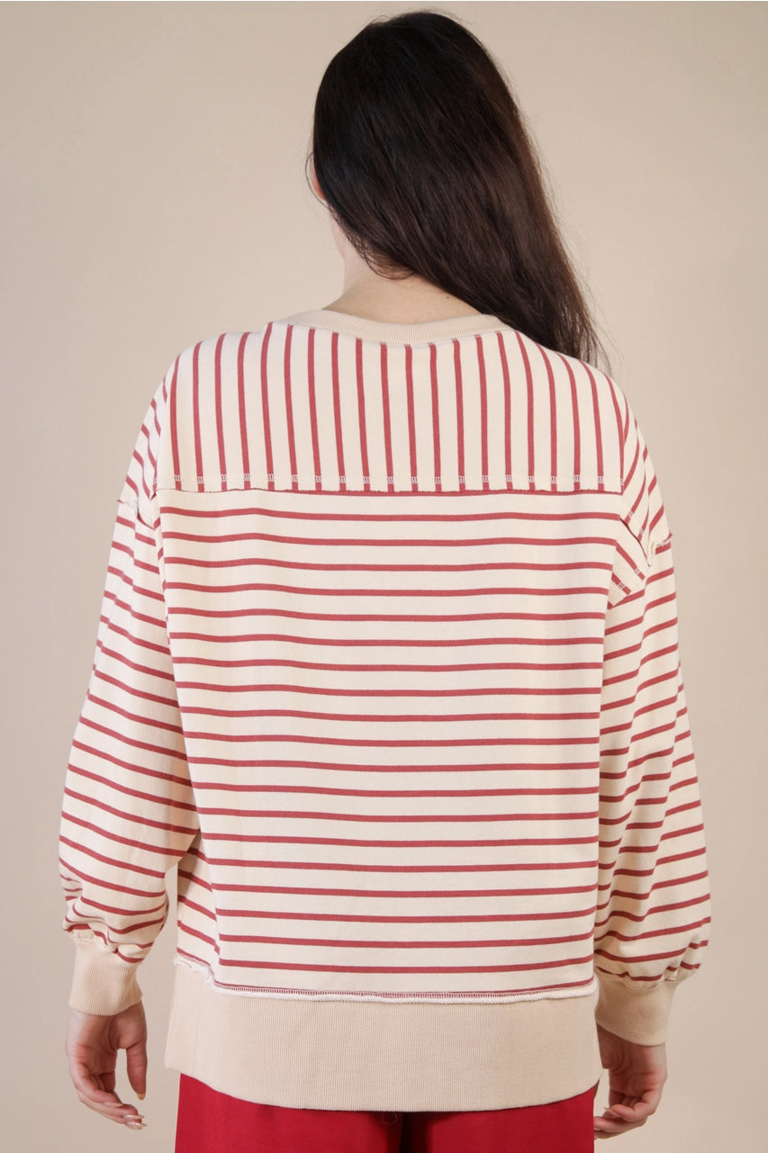 Back view: “Back of beige and brick striped oversized knit top showing mixed horizontal and vertical stripes with ribbed hem and cuffs.”