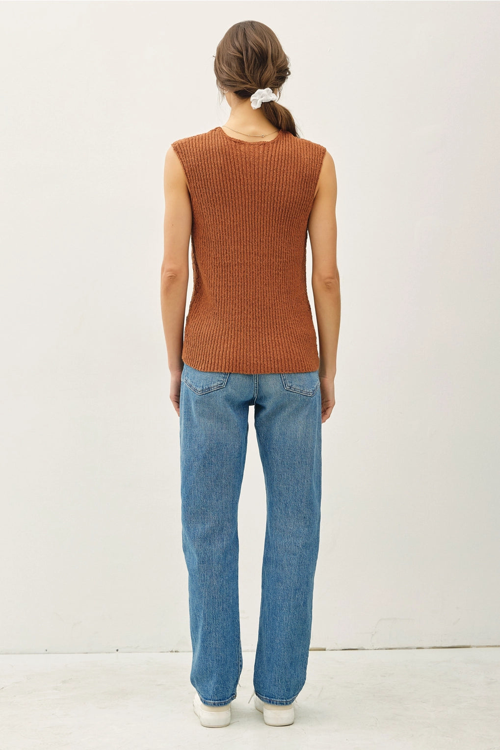 Back view Person wearing a brown sleeveless sweater and blue jeans on a white background