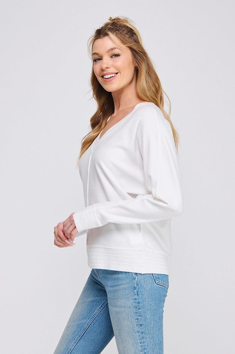 Woman wearing a white sweater and blue jeans on a plain background