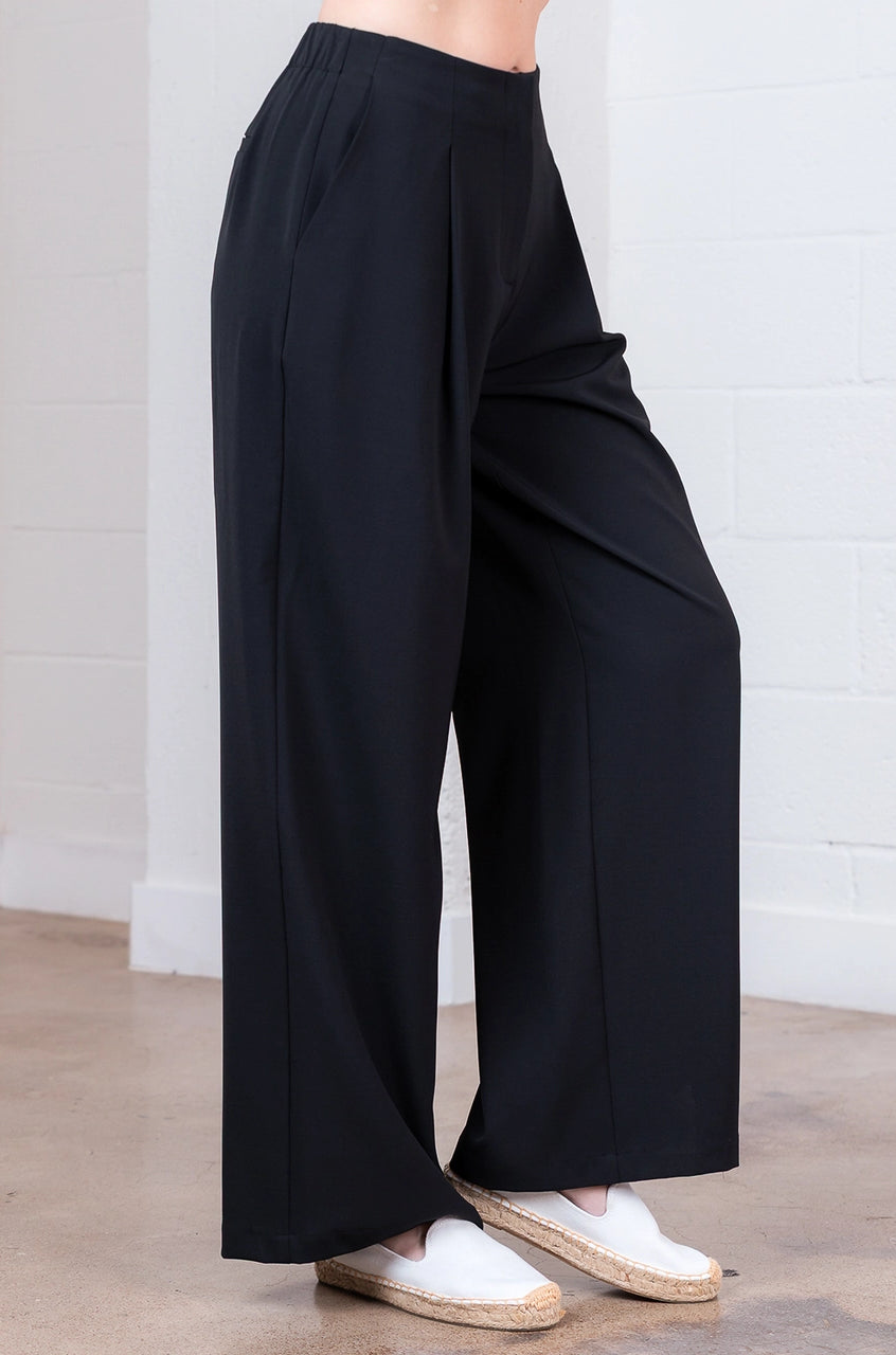 Person wearing black wide-leg pants with white shoes on a light wooden floor.