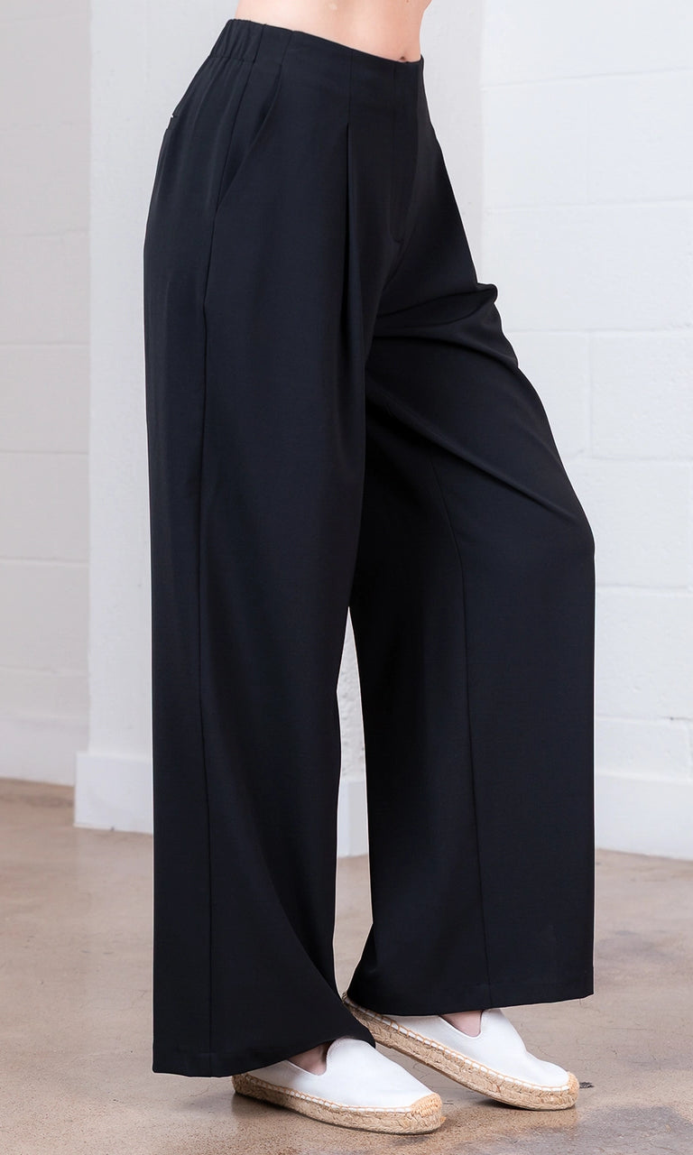 Person wearing black wide-leg pants with white shoes on a light wooden floor.