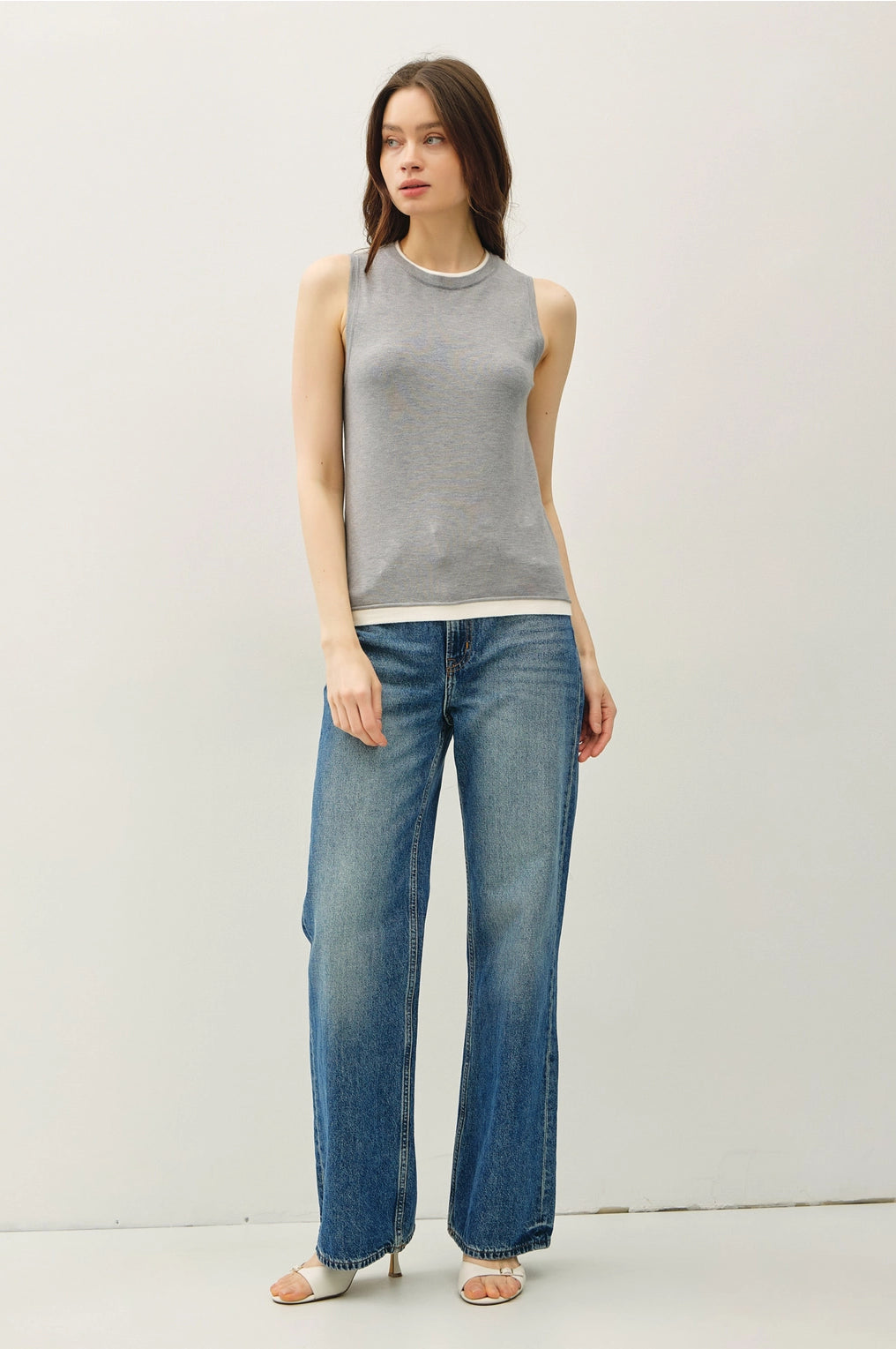 Woman wearing a gray sleeveless top and blue jeans against a white background