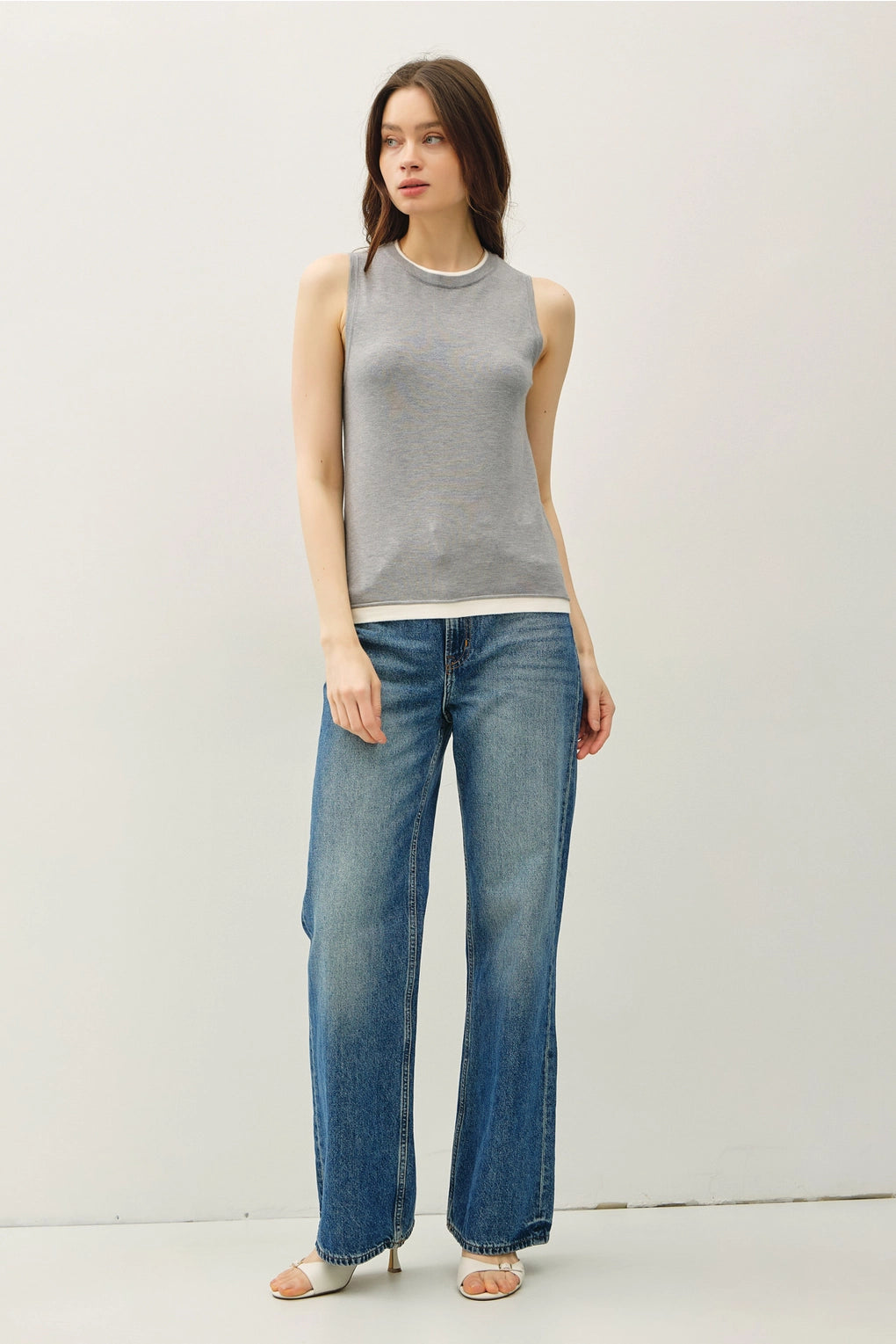 Woman wearing a gray sleeveless top and blue jeans against a white background