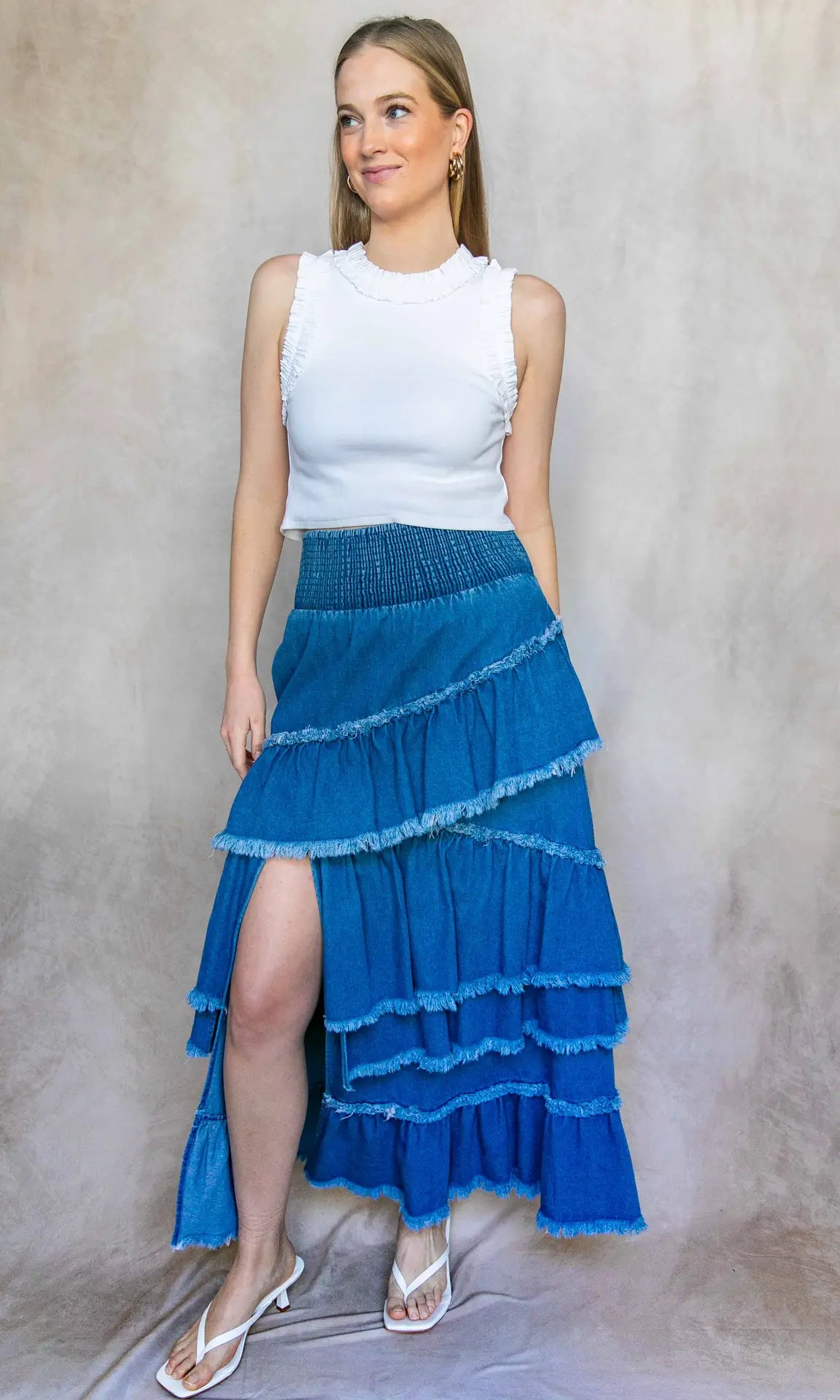Woman wearing a white top and blue tiered skirt against a neutral background