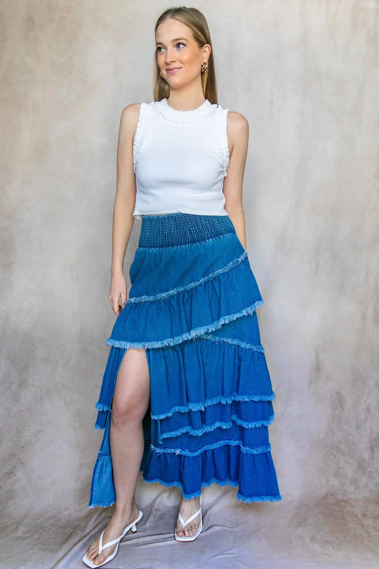 Woman wearing a white top and blue tiered skirt against a neutral background