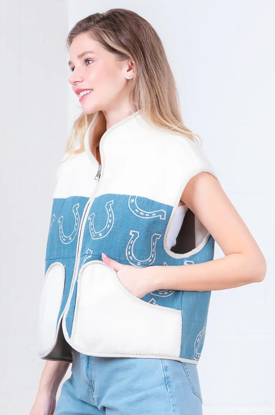 Model wearing indigo denim vest with white horseshoe print and faux-fur collar, zipped front, hands in pockets.”