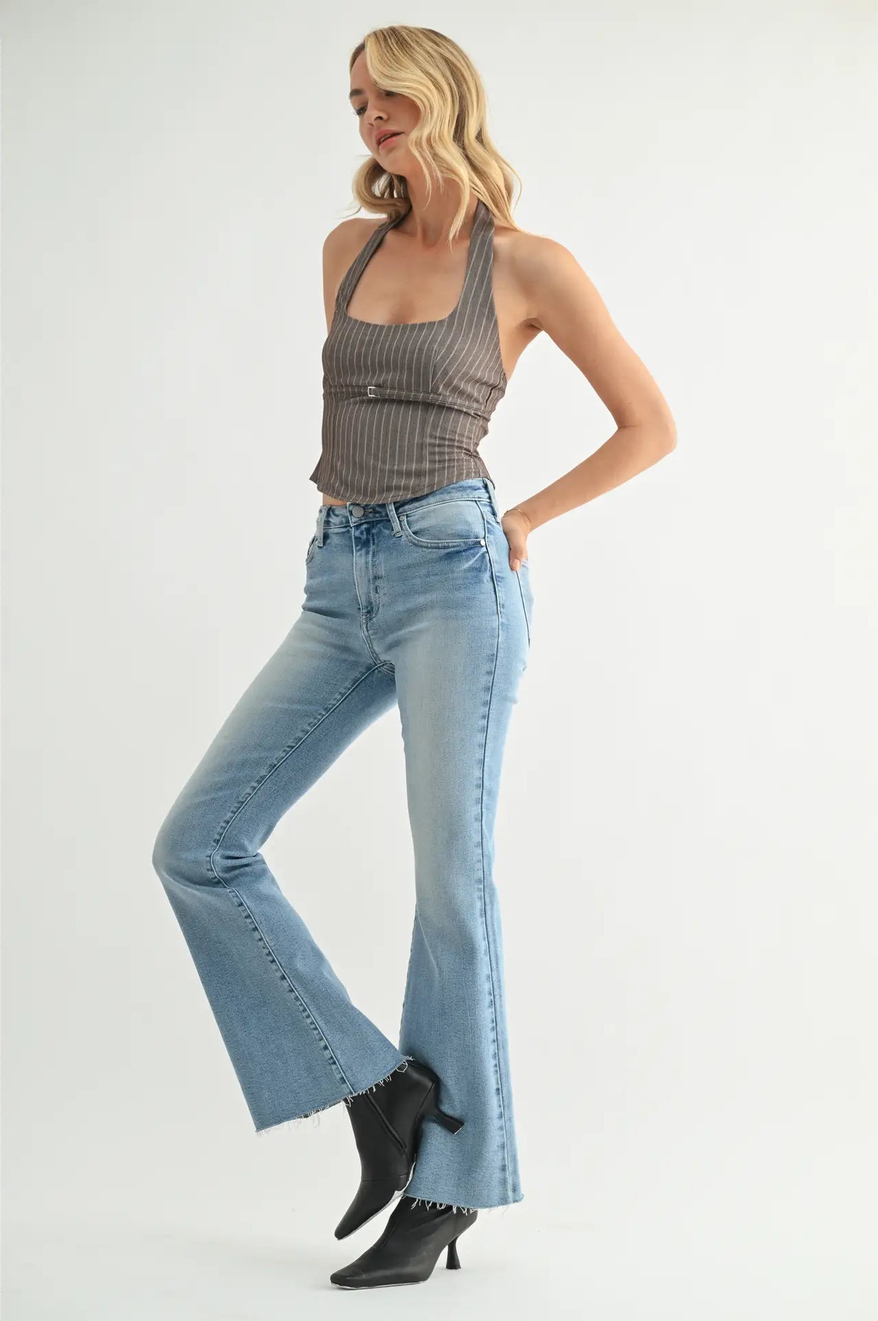 Woman wearing a gray halter top and blue flared jeans on a white background