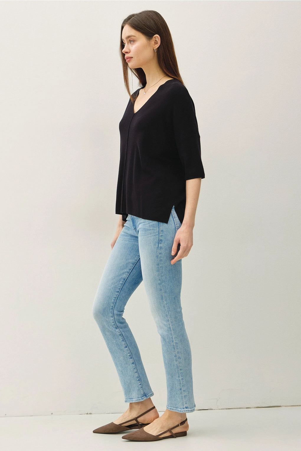 Woman wearing a black top and light blue jeans on a white background