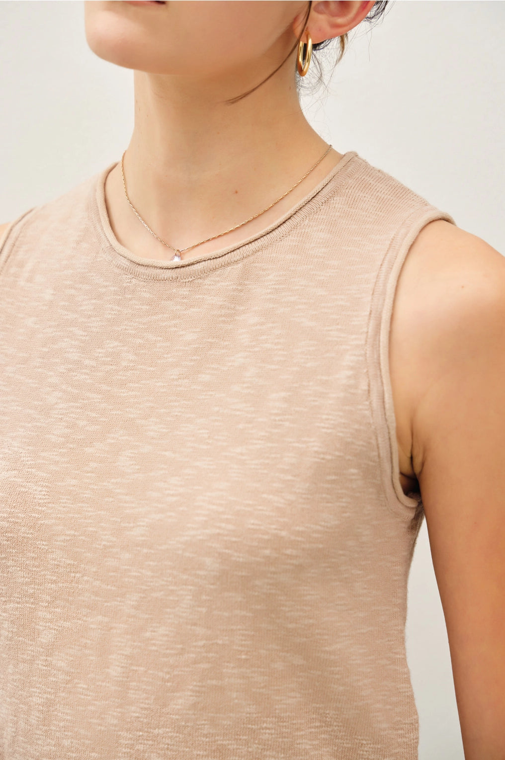 Beige sleeveless top worn by a person on a light gray background