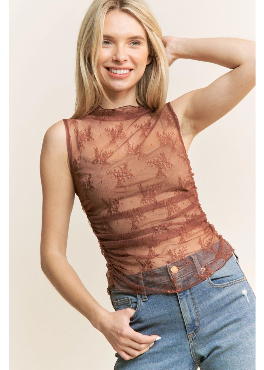 Woman wearing a brown lace top sleeveless high neck and light blue jeans indoors.