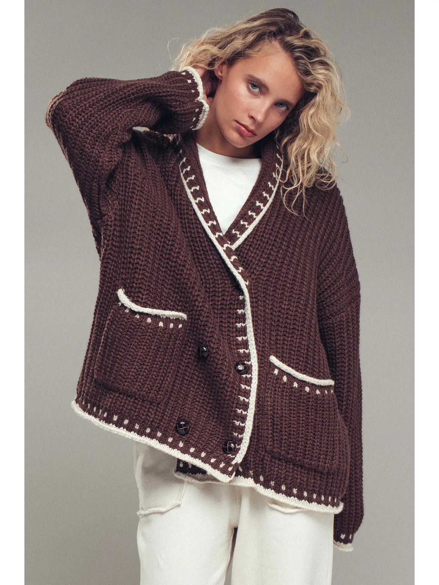 Woman wearing a brown knitted cardigan with white trim on a gray background