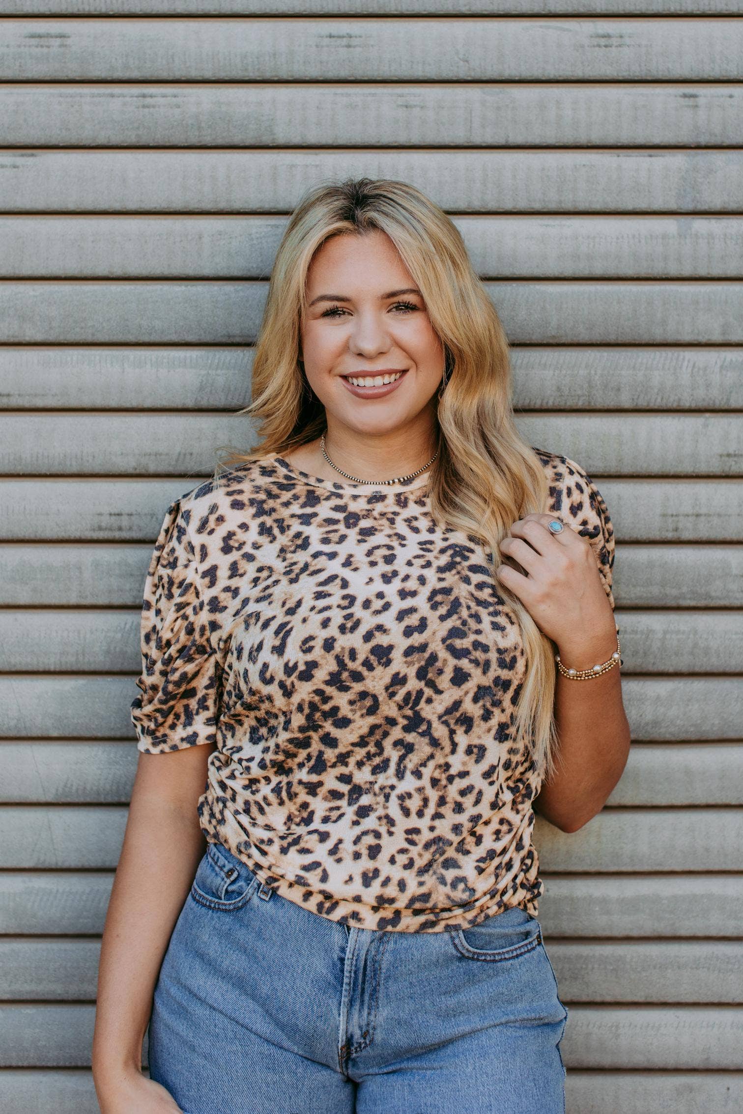 Woman wearing a leopard print top and blue jeans standing against a metallic background