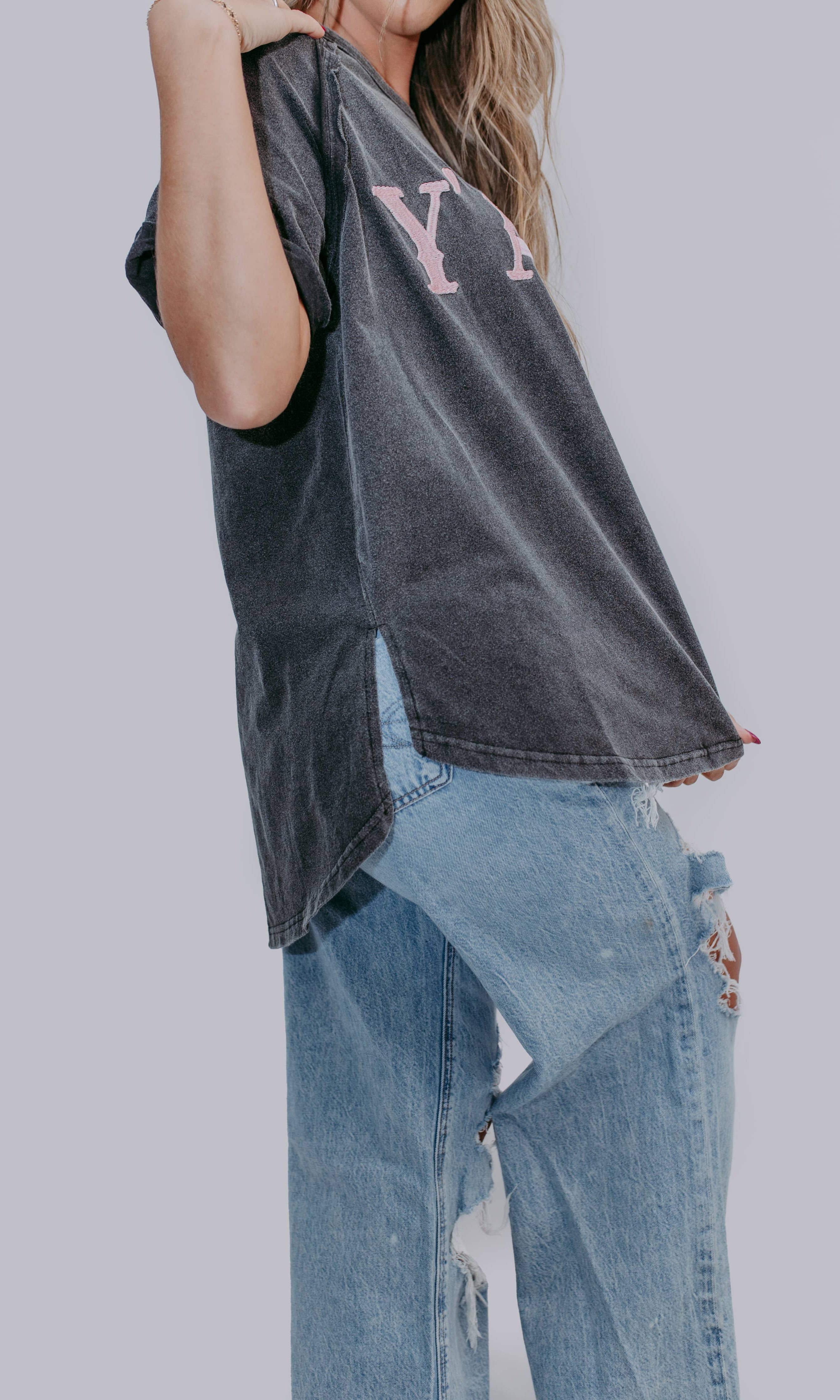 Person wearing a mineral gray short sleeve shirt with lettering and ripped jeans on a plain background