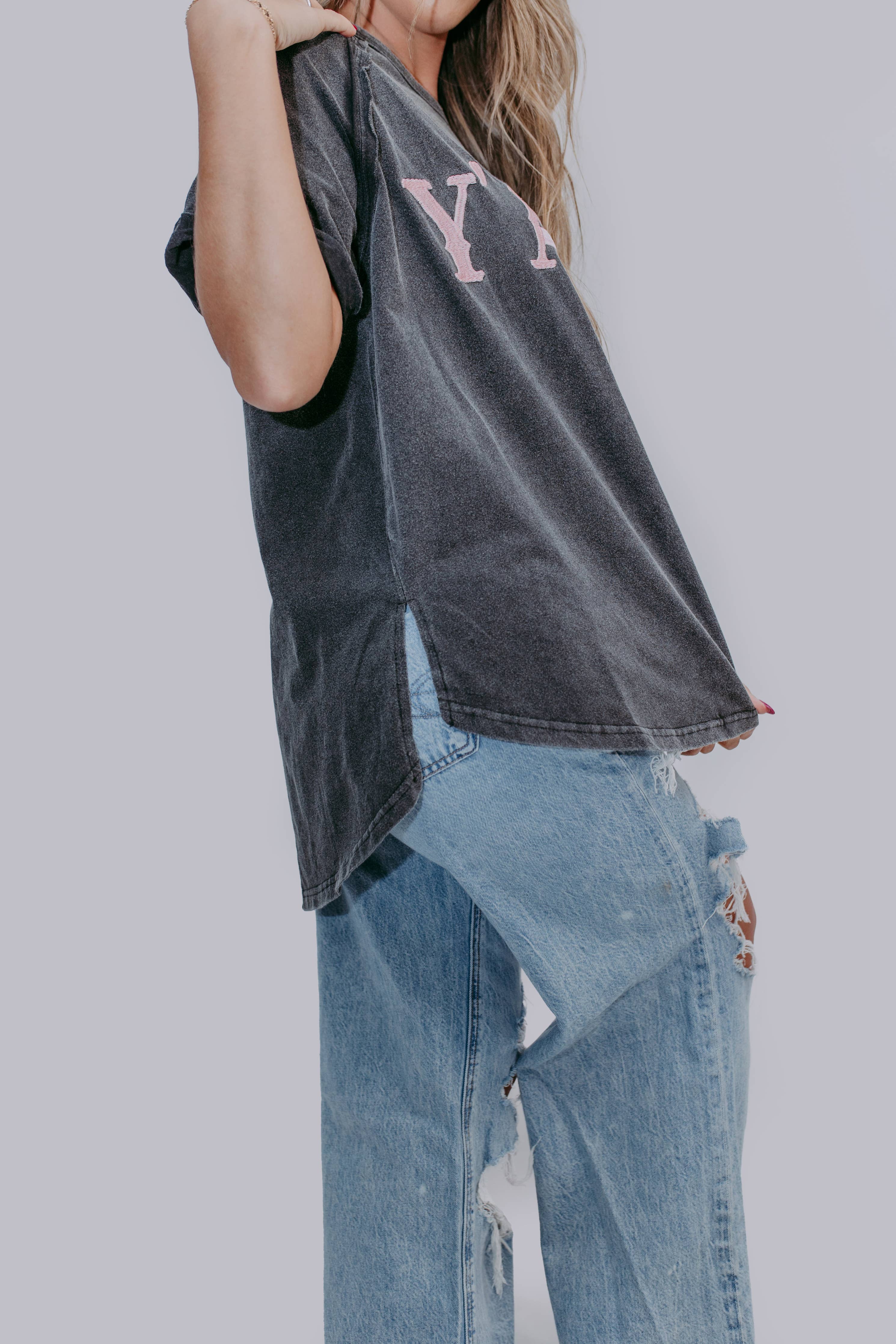 Person wearing a mineral gray short sleeve shirt with lettering and ripped jeans on a plain background