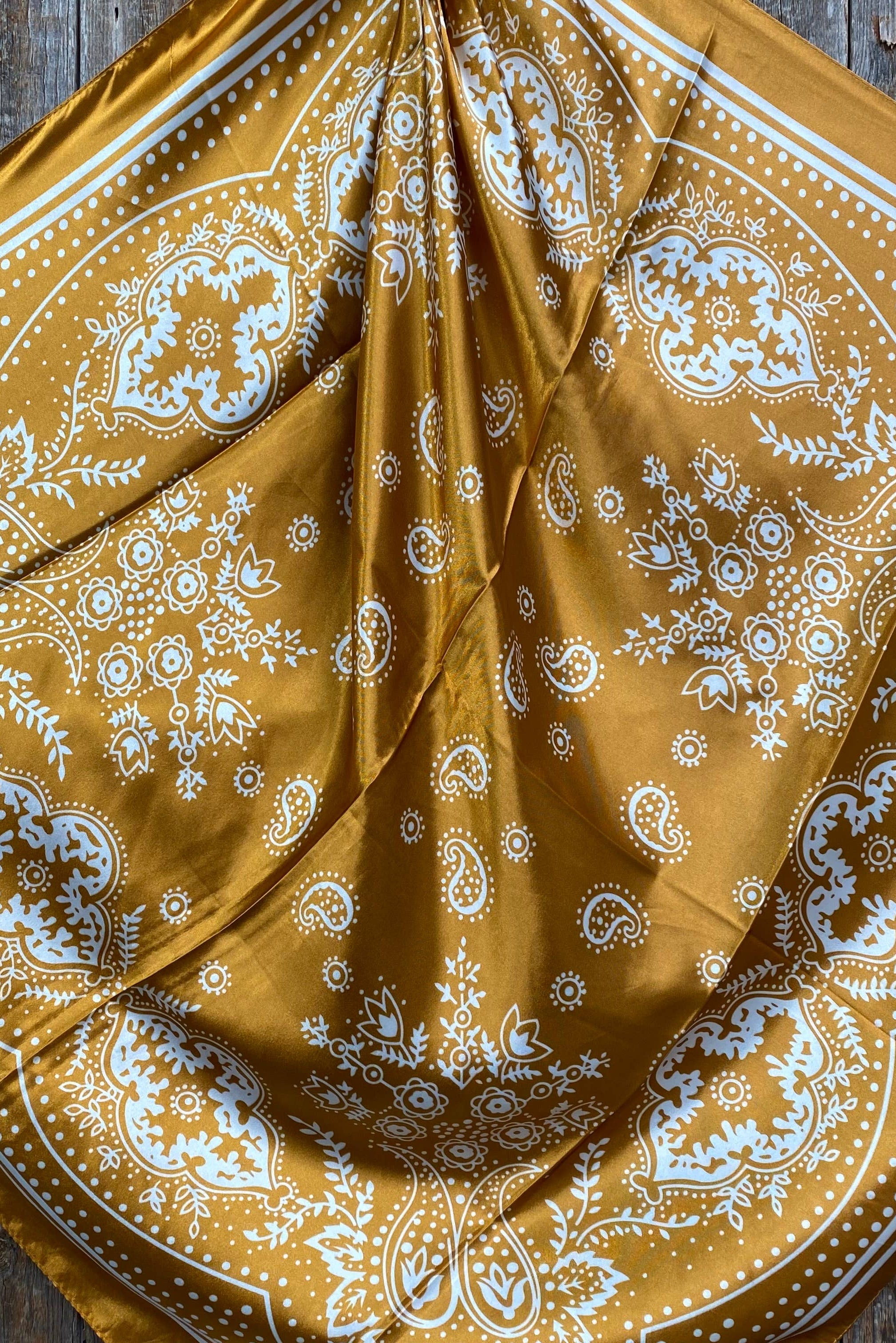 Yellow mustard bandana with white paisley patterns on a wooden surface