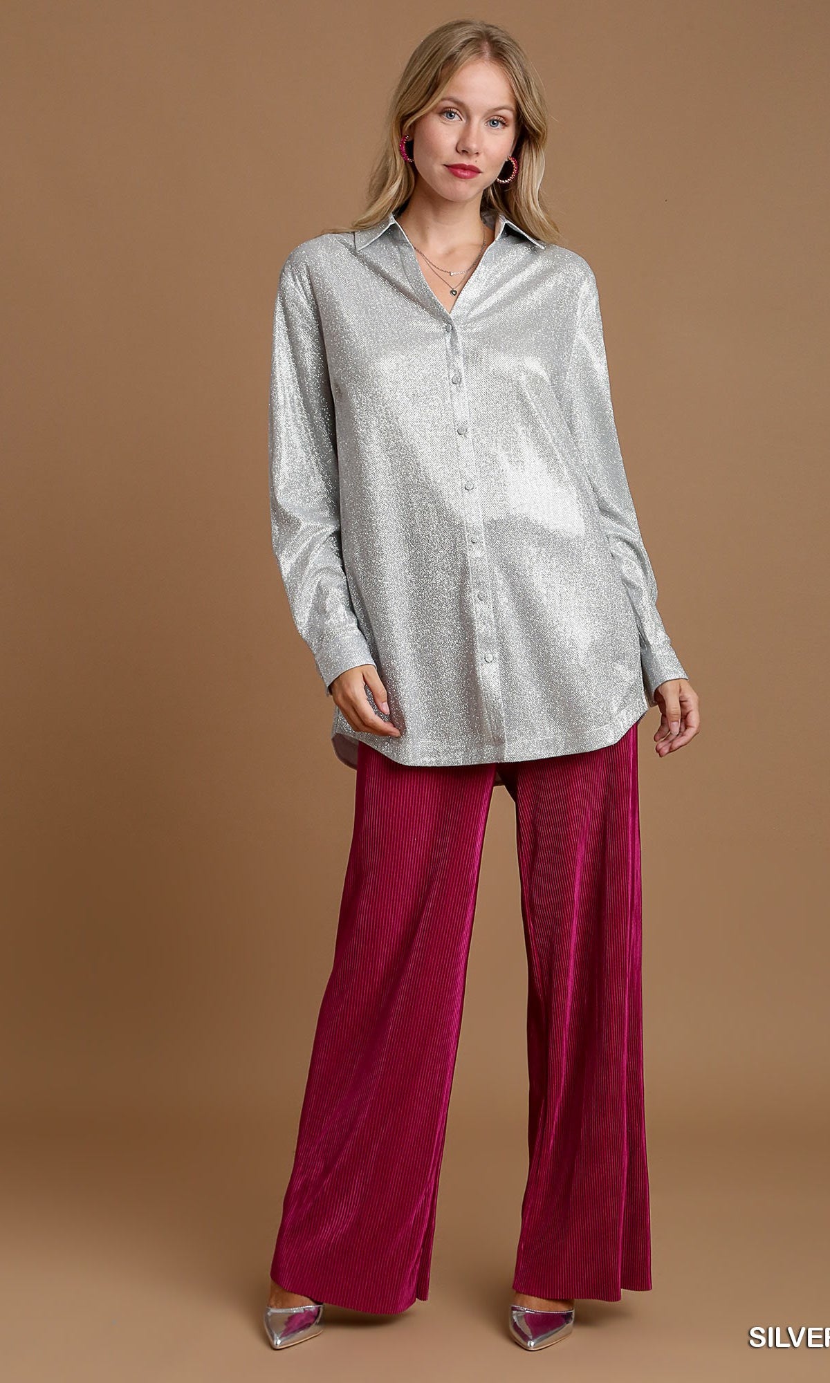 Woman wearing a silver button-up shirt and magenta pants on a brown background