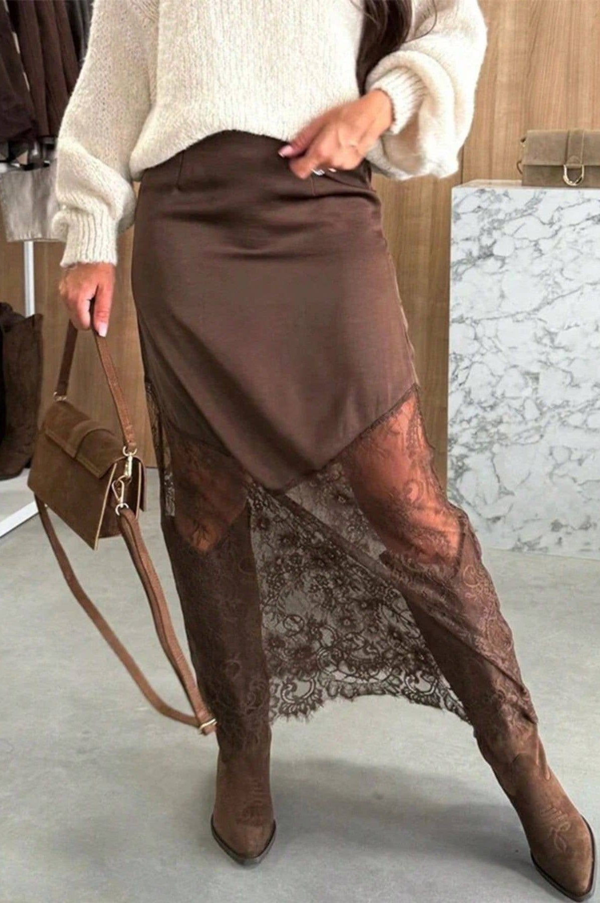 Person wearing a brown skirt with lace detailing and brown boots, holding a brown handbag.
