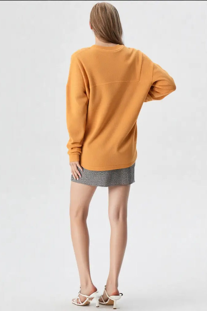 Person wearing a mustard yellow sweater and gray skirt on a white background