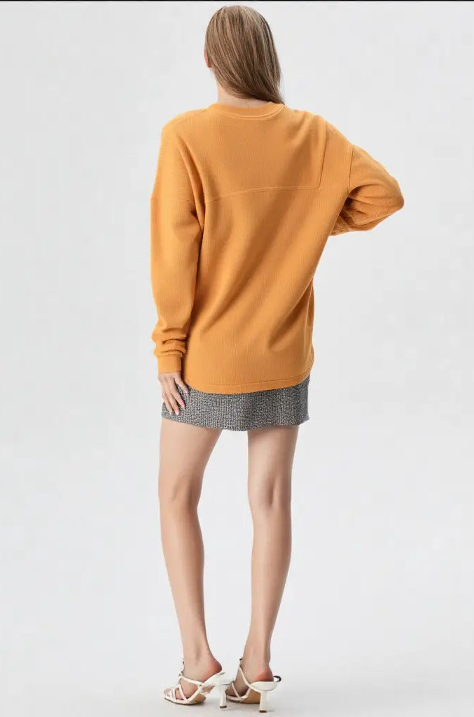 Person wearing a mustard yellow sweater and gray skirt on a white background