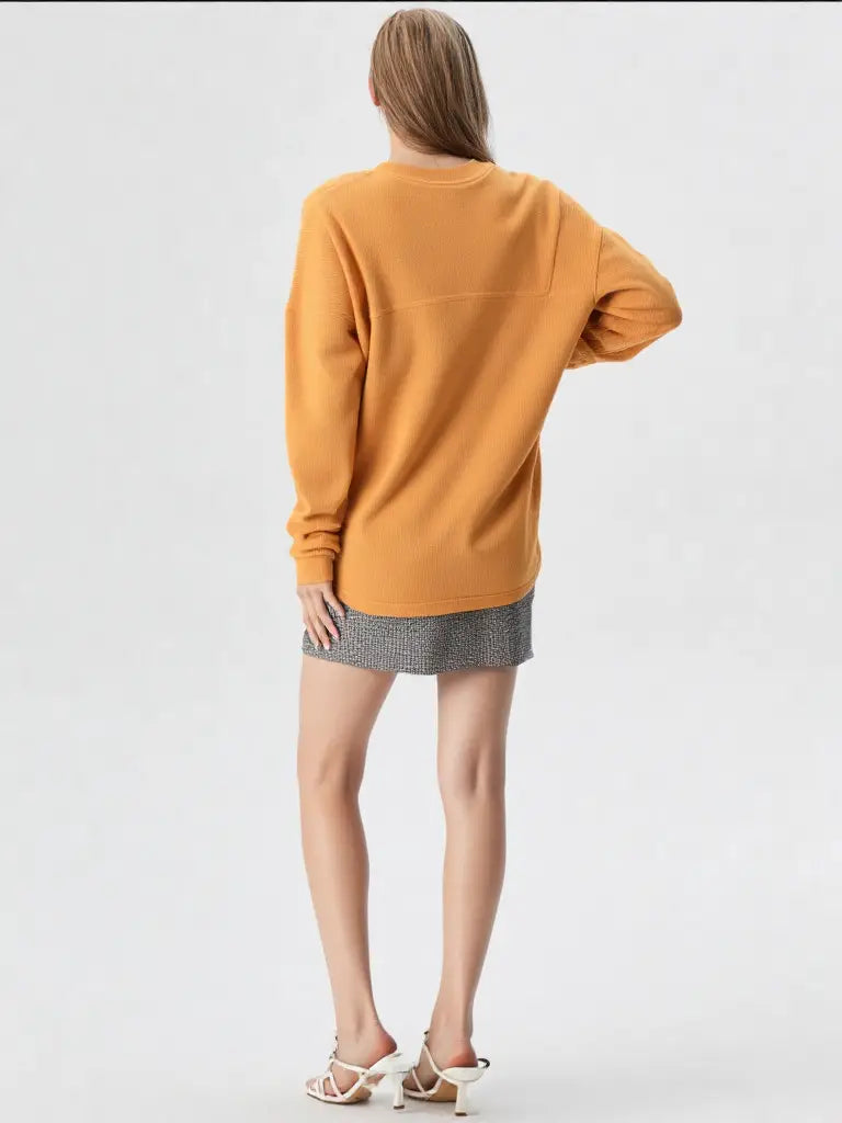 Person wearing a mustard yellow sweater and gray skirt on a white background