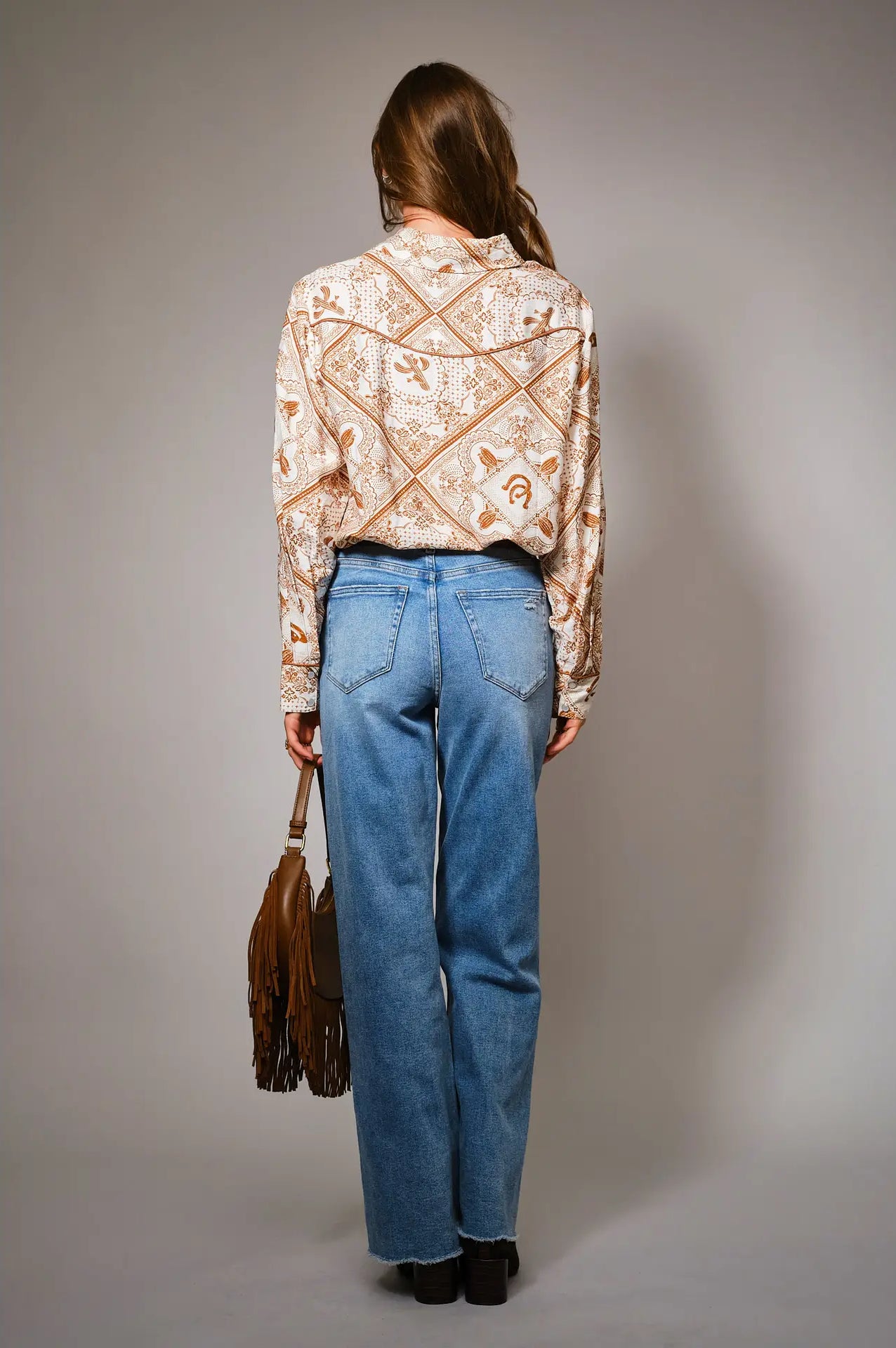 Person wearing a patterned blouse and blue jeans, standing against a plain background
