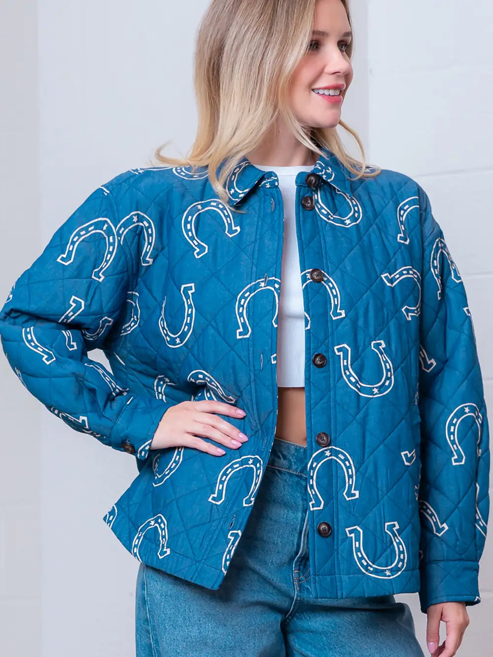 Front view of denim-blue quilted jacket with white horseshoe print and button front on model.