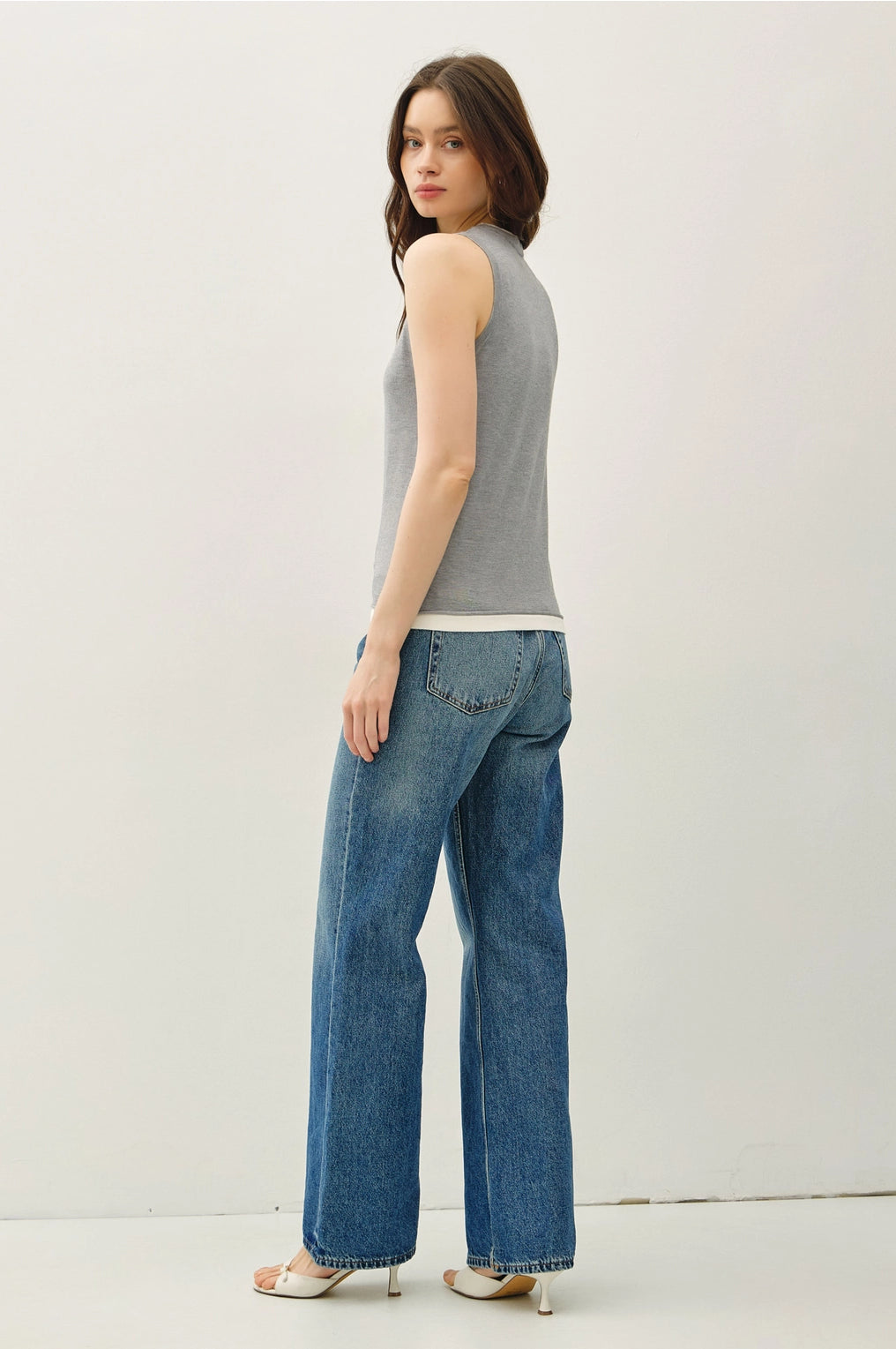 Woman wearing a gray sleeveless top and blue jeans on a white background