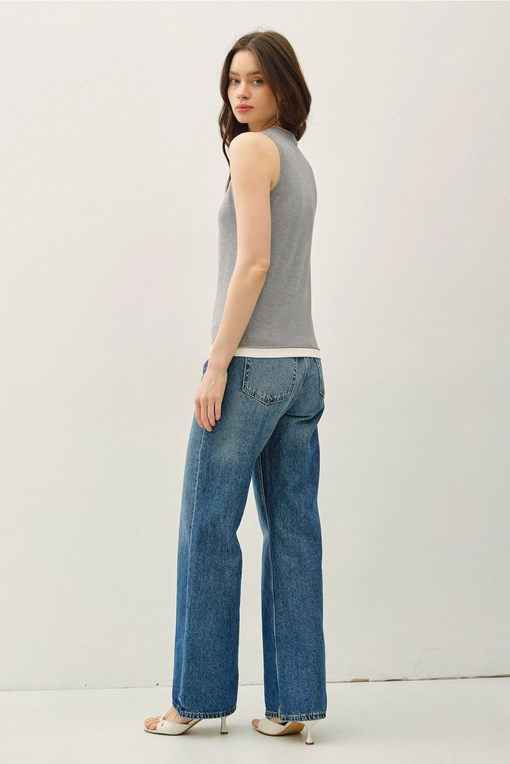 Woman wearing a gray sleeveless top and blue jeans on a white background