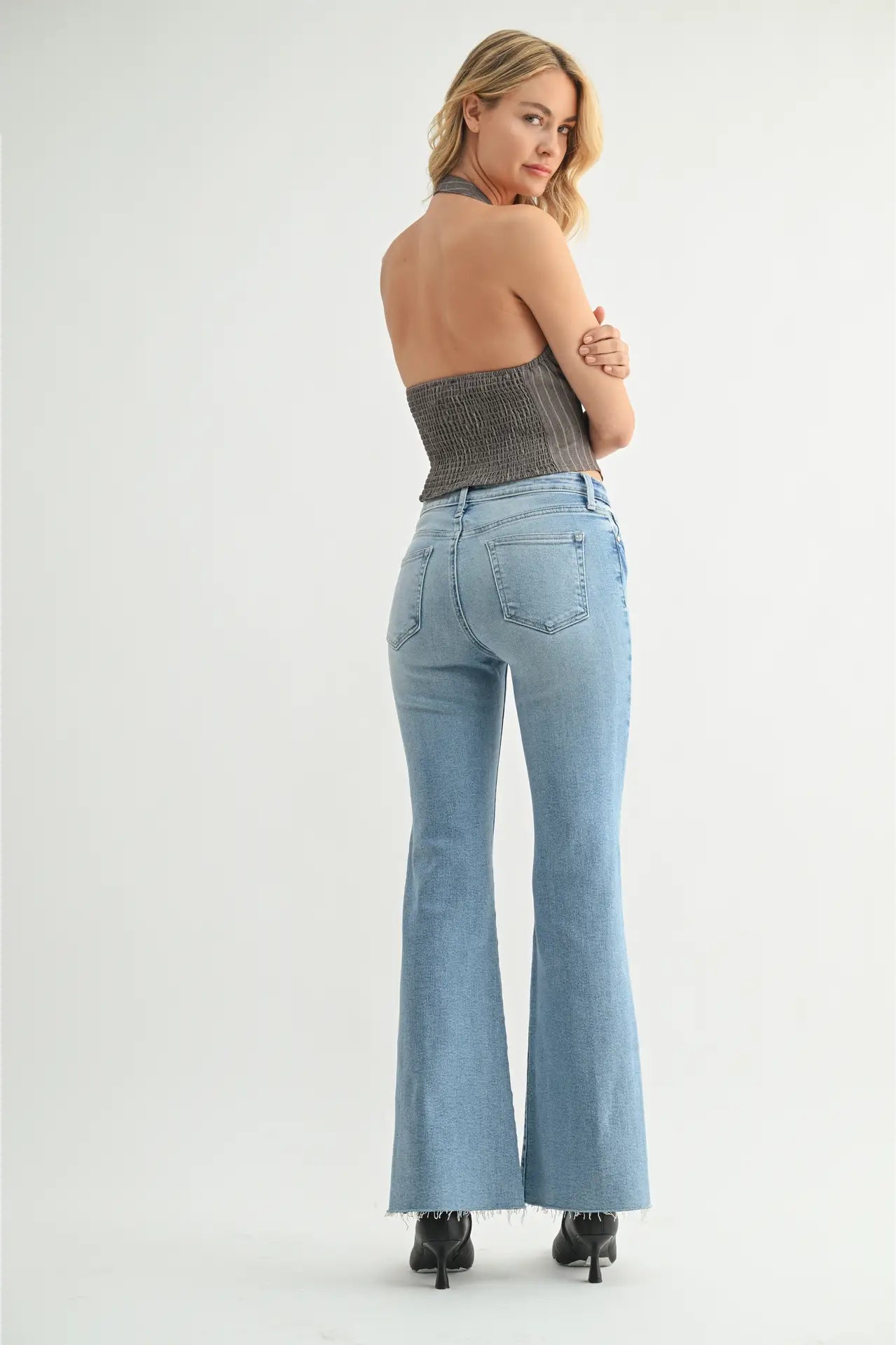 Woman wearing light blue flared jeans and a strapless top on a white background