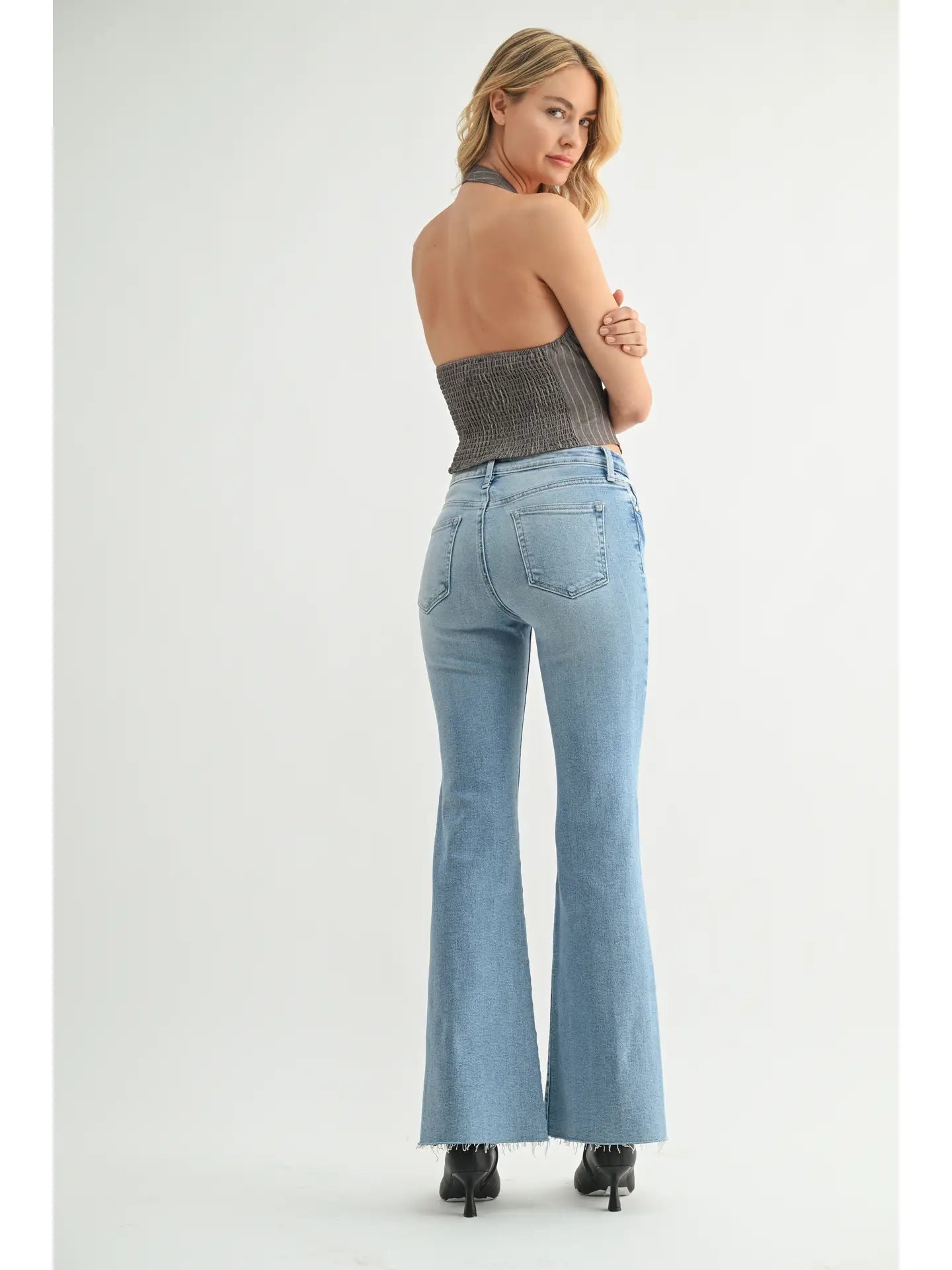 Woman wearing light blue flared jeans and a strapless top on a white background