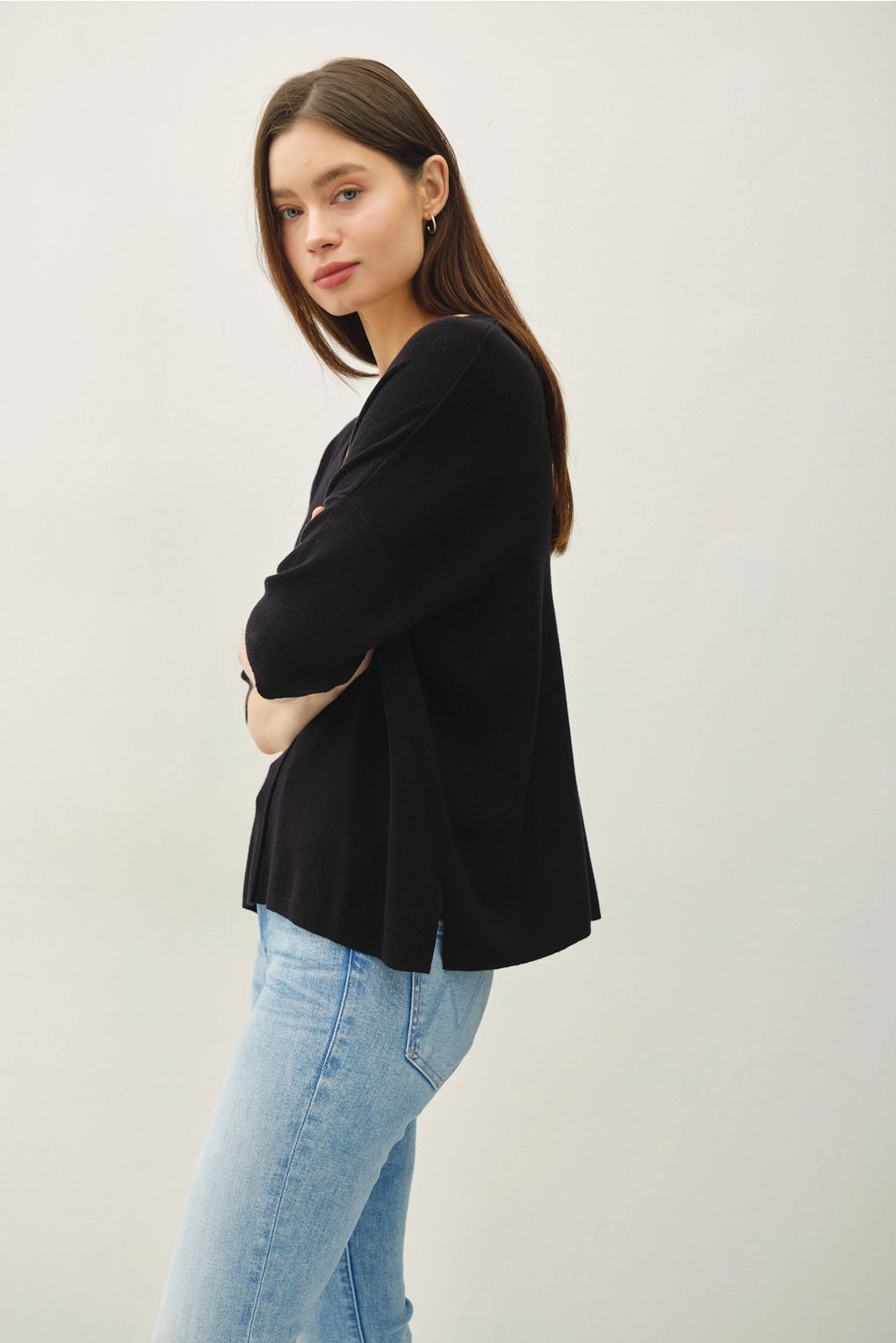 Woman wearing a black top and light blue jeans against a white background