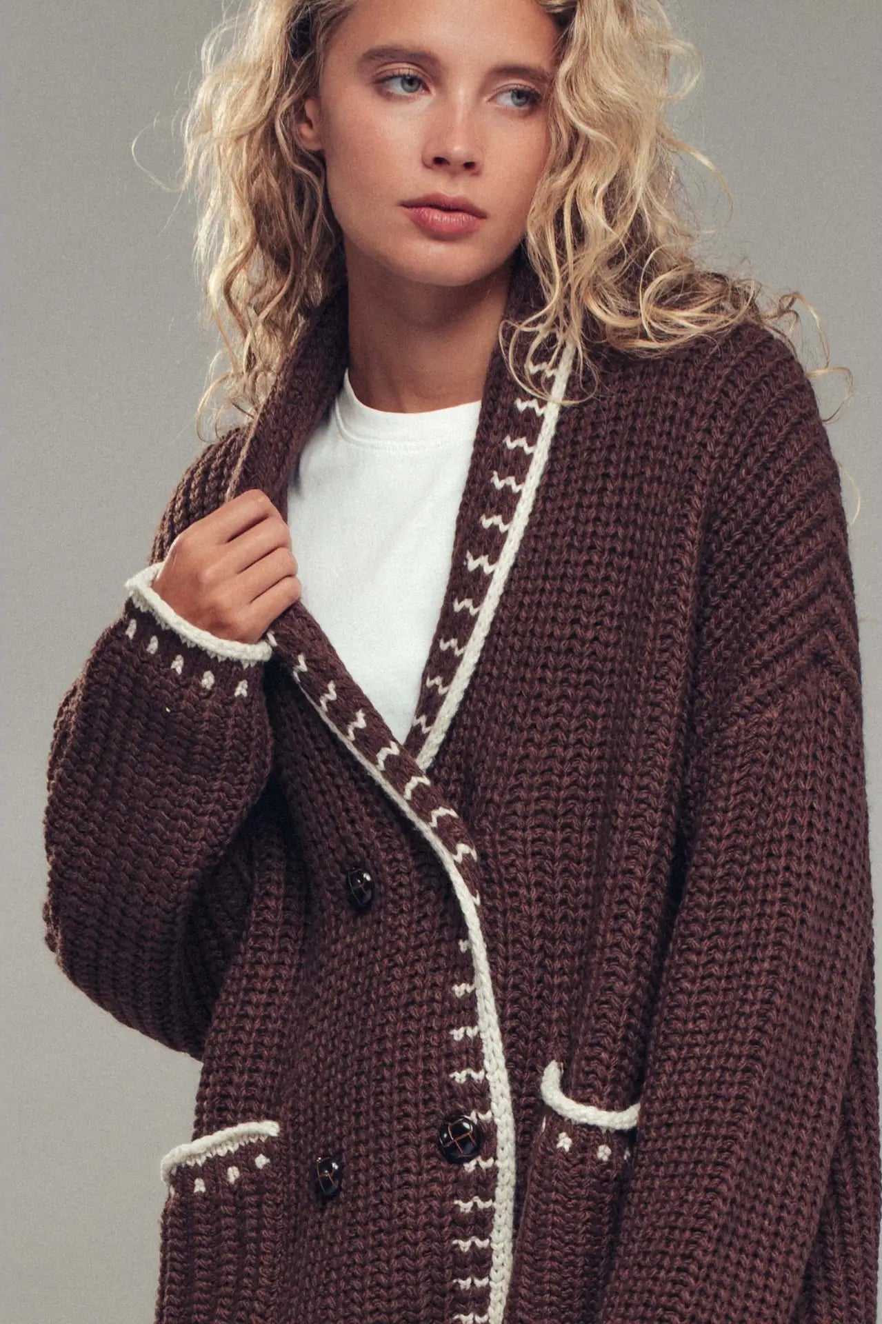 Woman wearing a brown knitted coat with white trim against a gray background