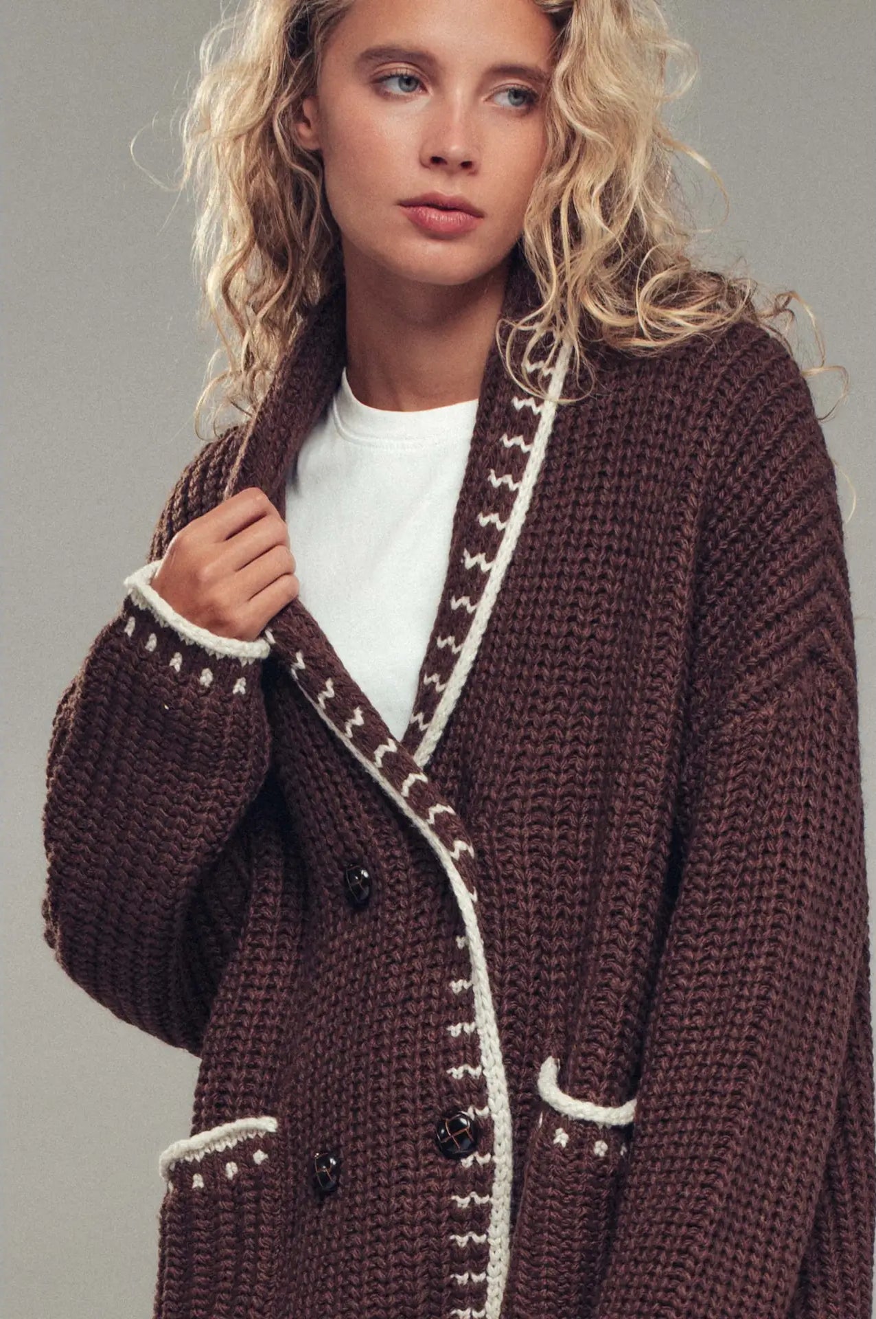 Woman wearing a brown knitted coat with white trim against a gray background