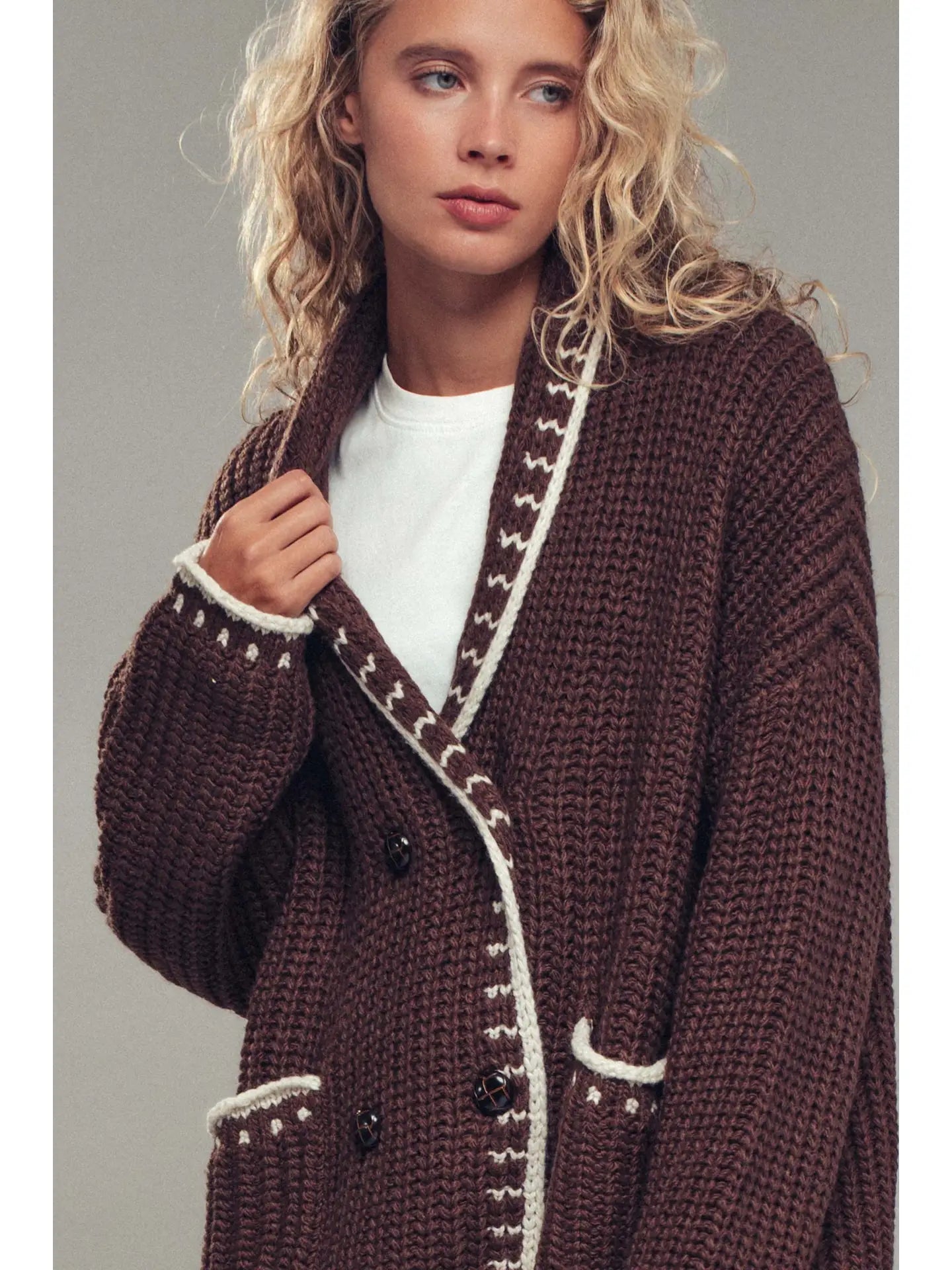 Woman wearing a brown knitted coat with white trim against a gray background