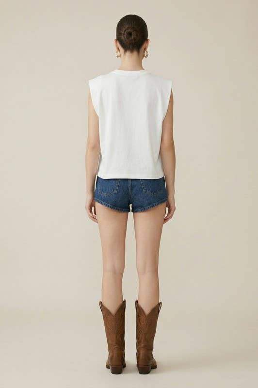 Person wearing a white sleeveless top, blue denim shorts, and brown cowboy boots on a plain background