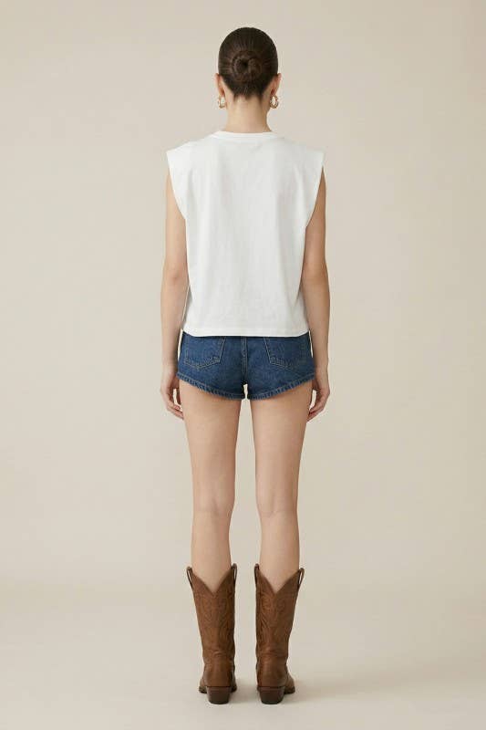 Person wearing a white sleeveless top, blue denim shorts, and brown cowboy boots on a plain background