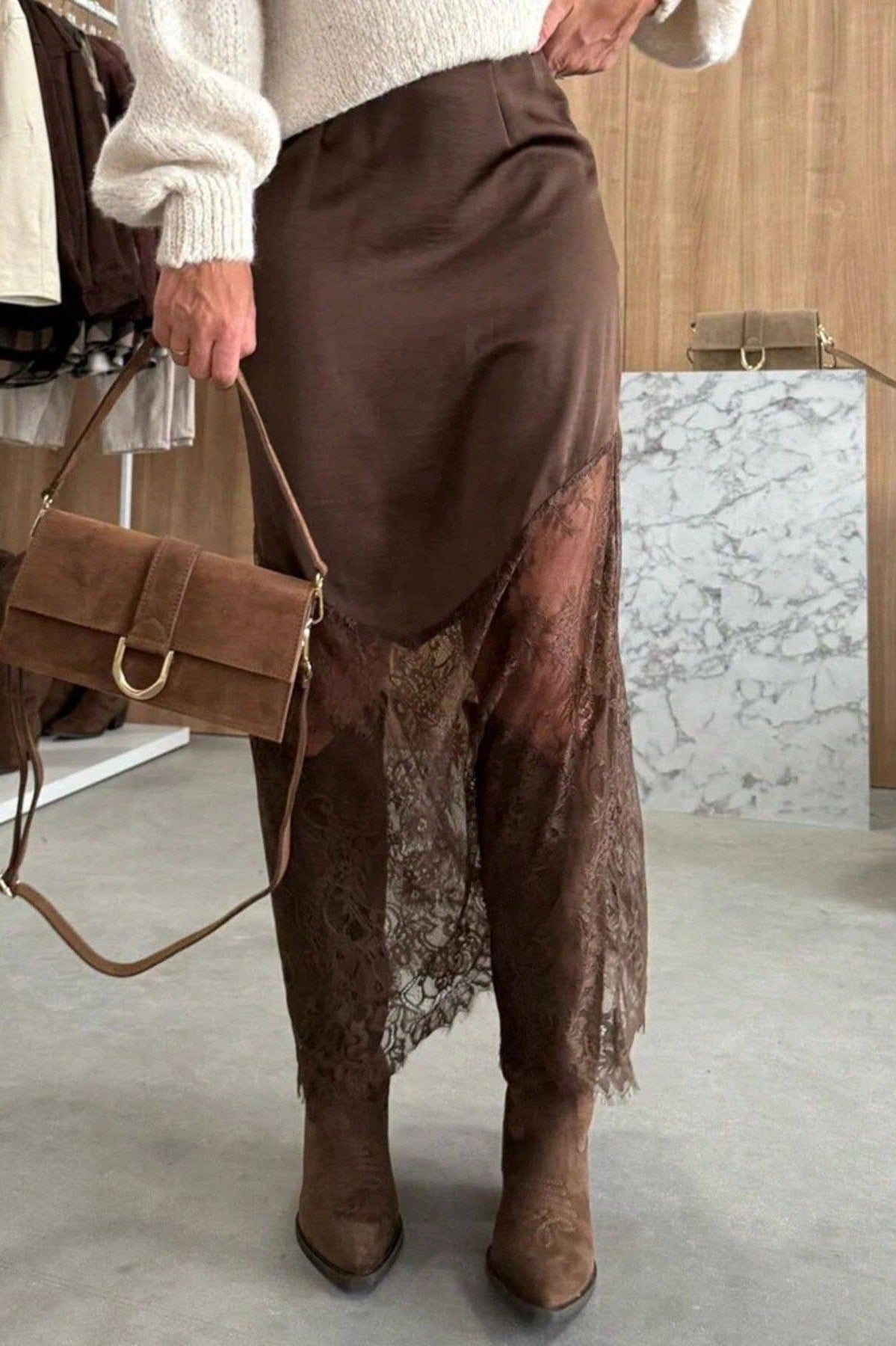 Person wearing brown skirt and boots holding a brown handbag indoors.