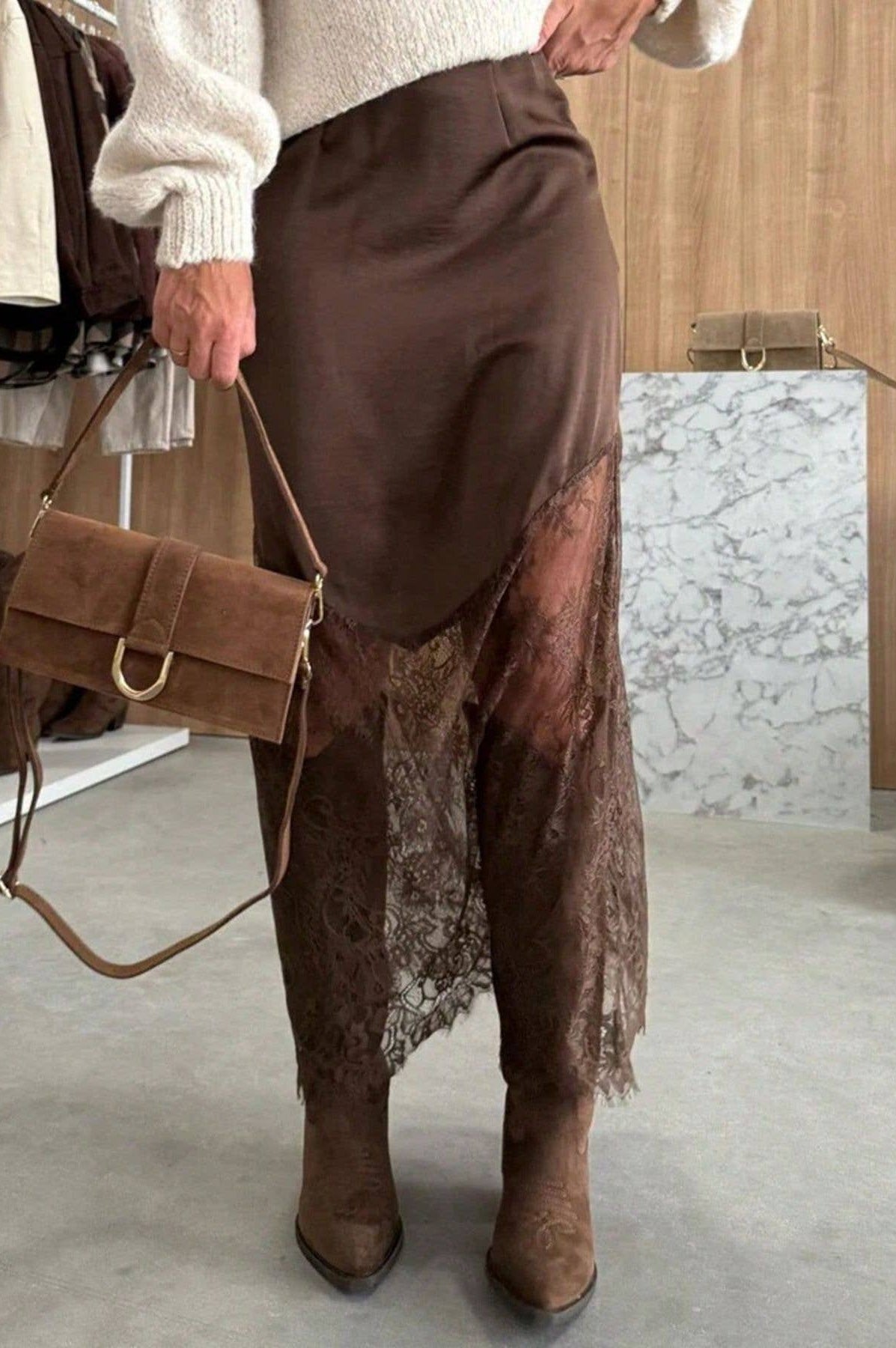 Person wearing brown skirt and boots holding a brown handbag indoors.