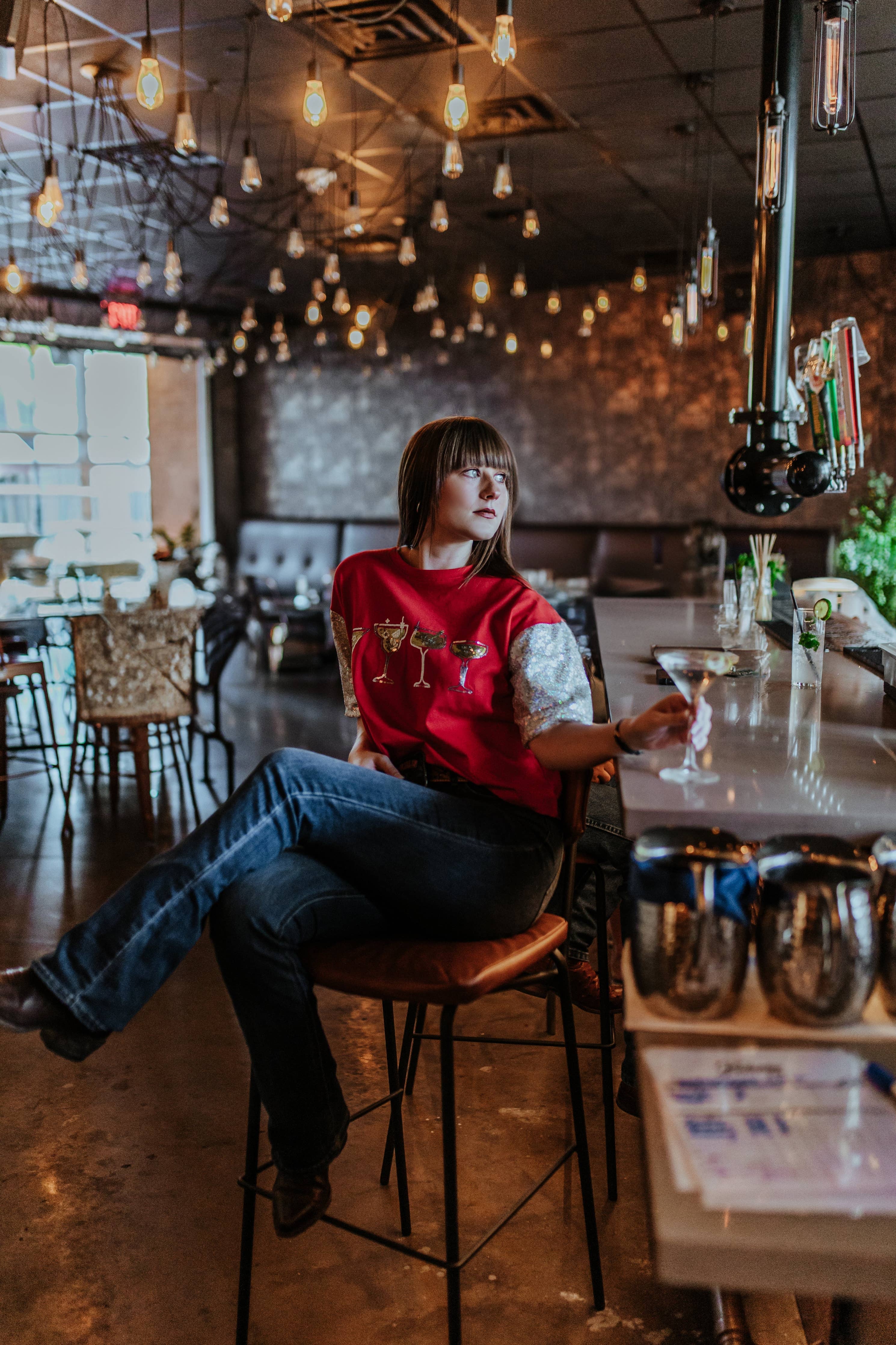 Person sitting at a bar counter in a dimly lit room with hanging lights.